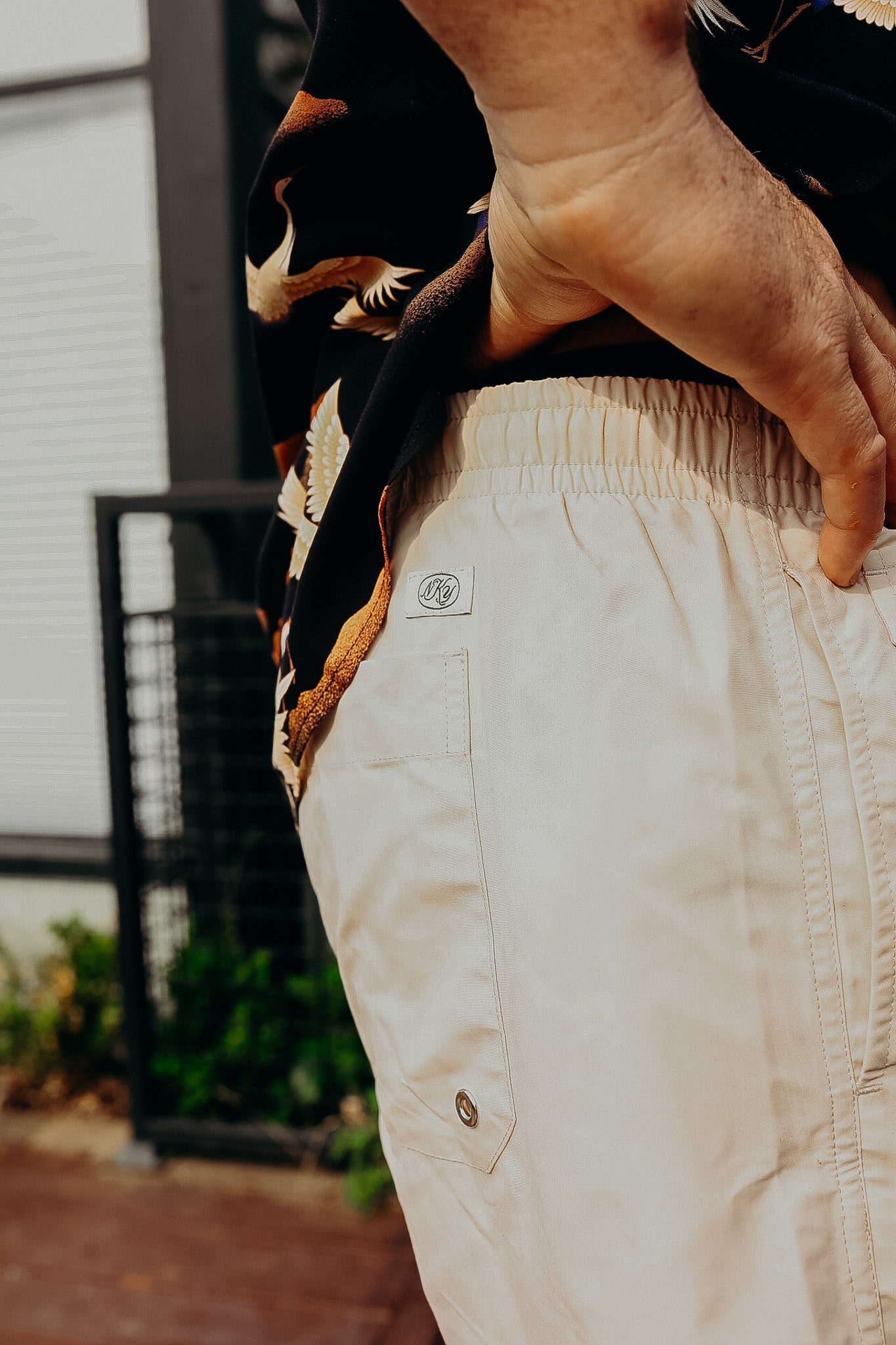 Close-up of man wearing beige casual shorts with back pocket and elastic waistband, black shirt with bird print outdoors