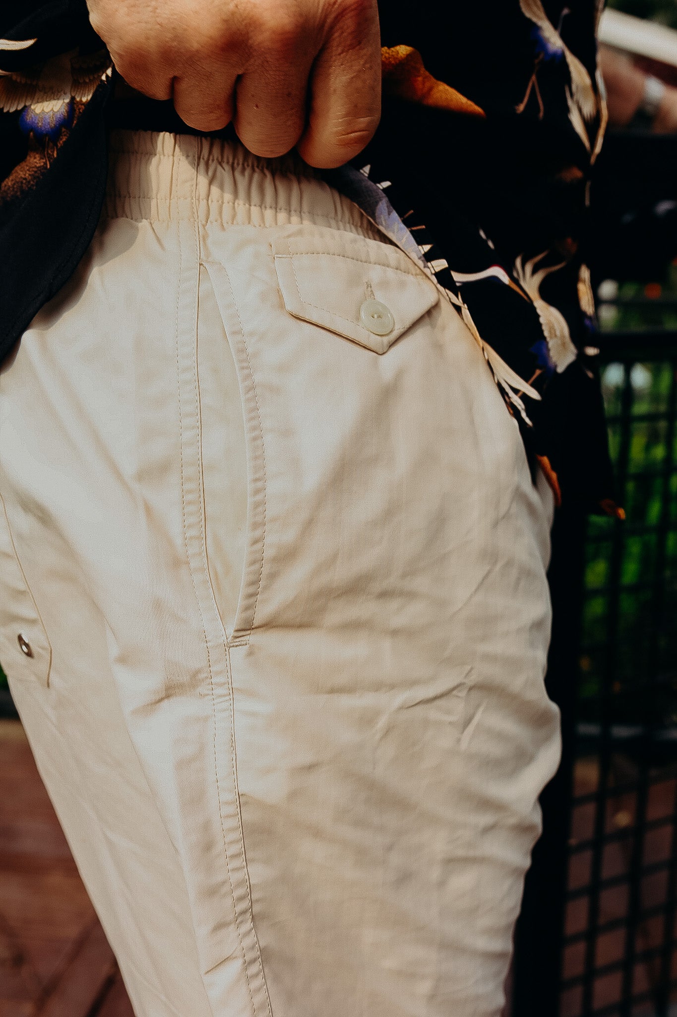 Close-up of beige casual pants pocket and waistband with button detail, worn with floral shirt at Iron Shop Provisions
