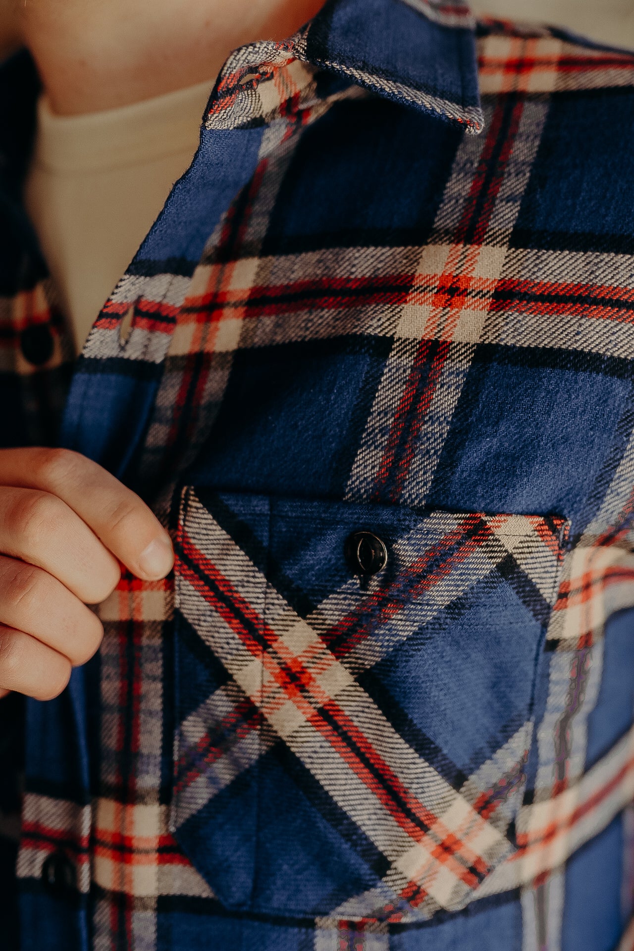 Close-up of hand holding the pocket flap of a blue and red plaid flannel shirt from Iron Shop Provisions