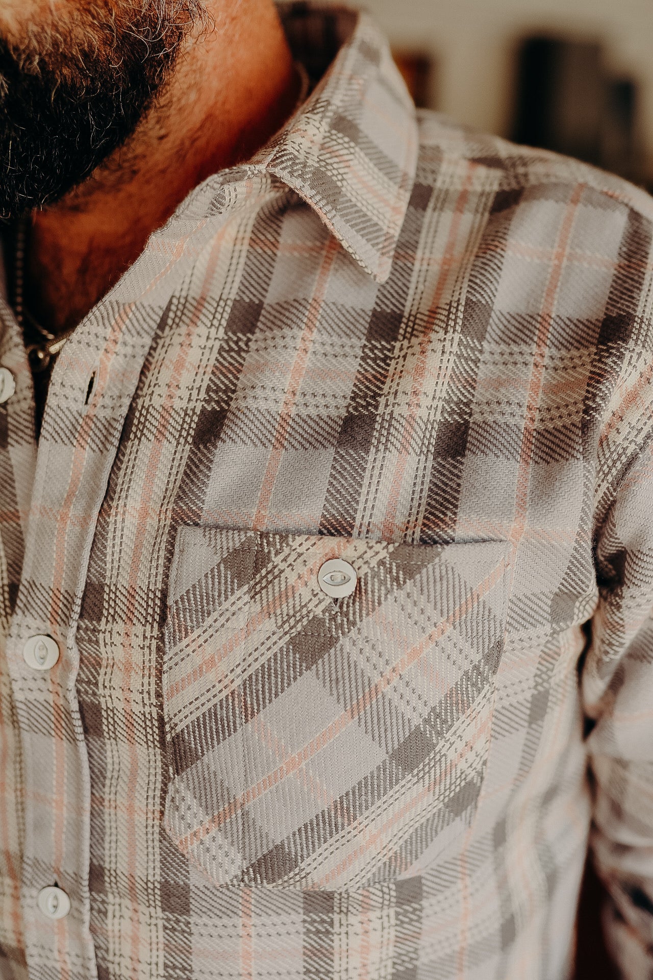 Close-up of a man wearing a beige and brown plaid button-up shirt from Iron Shop Provisions