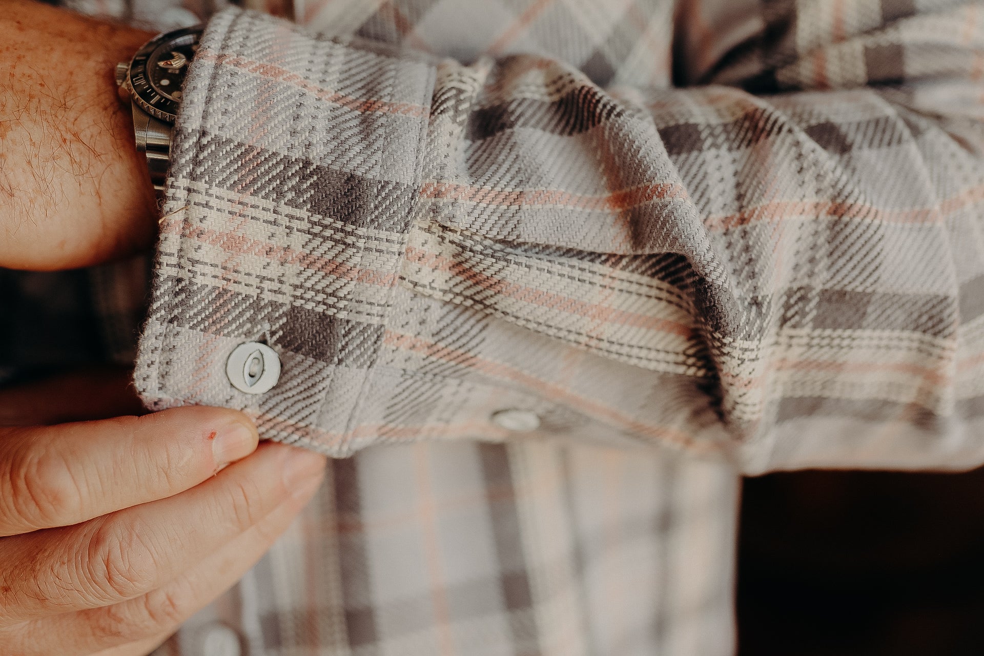 Close-up of a hand adjusting the cuff of a plaid shirt with a silver wristwatch visible under the sleeve