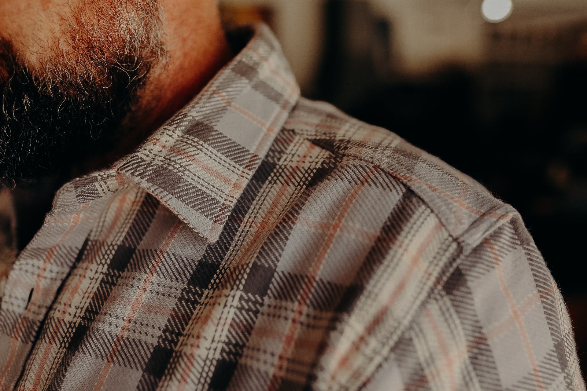 Close-up of a man wearing a brown and gray plaid shirt with beard, indoors, rustic style