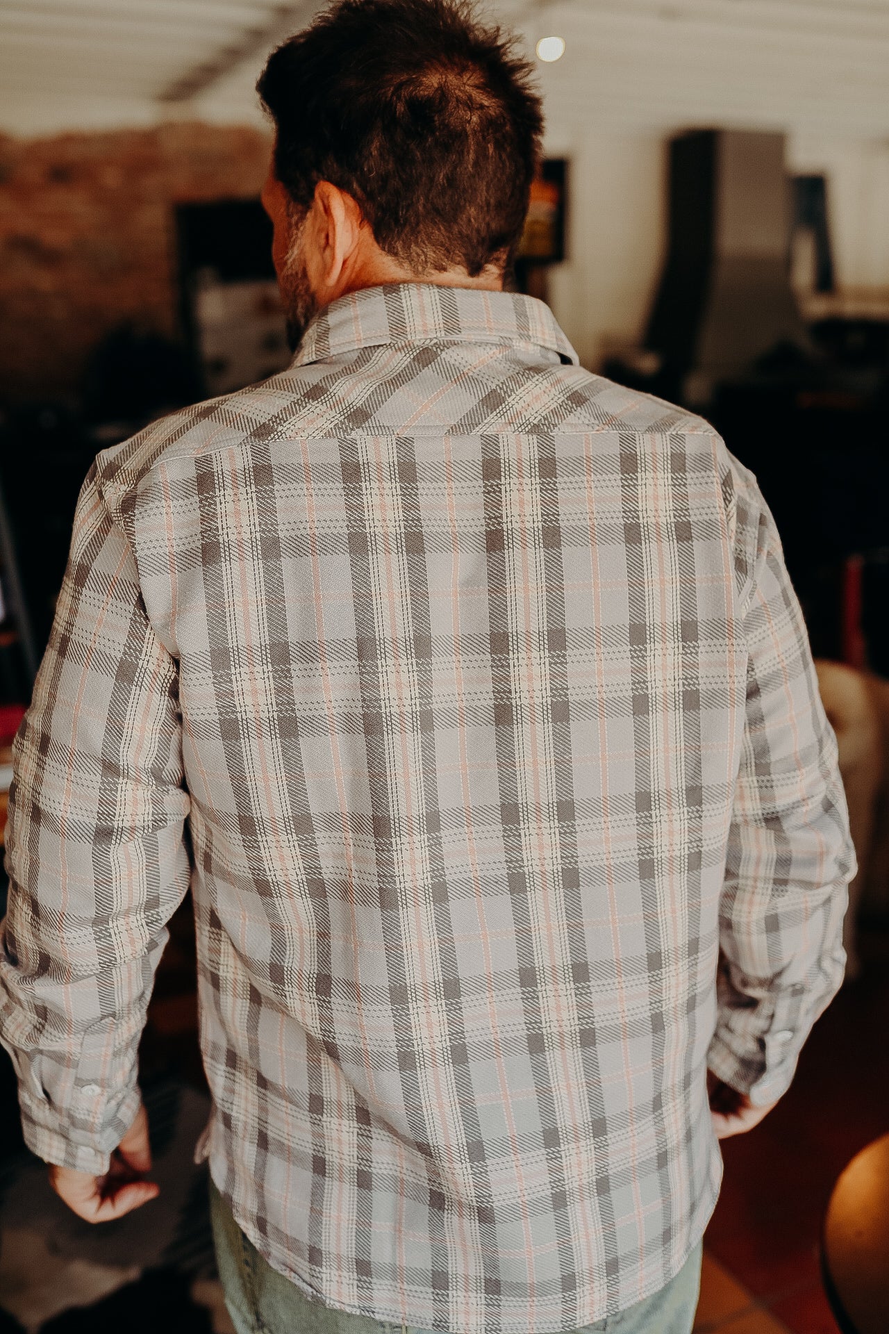 Back view of man wearing gray and white plaid shirt indoors with rustic decor