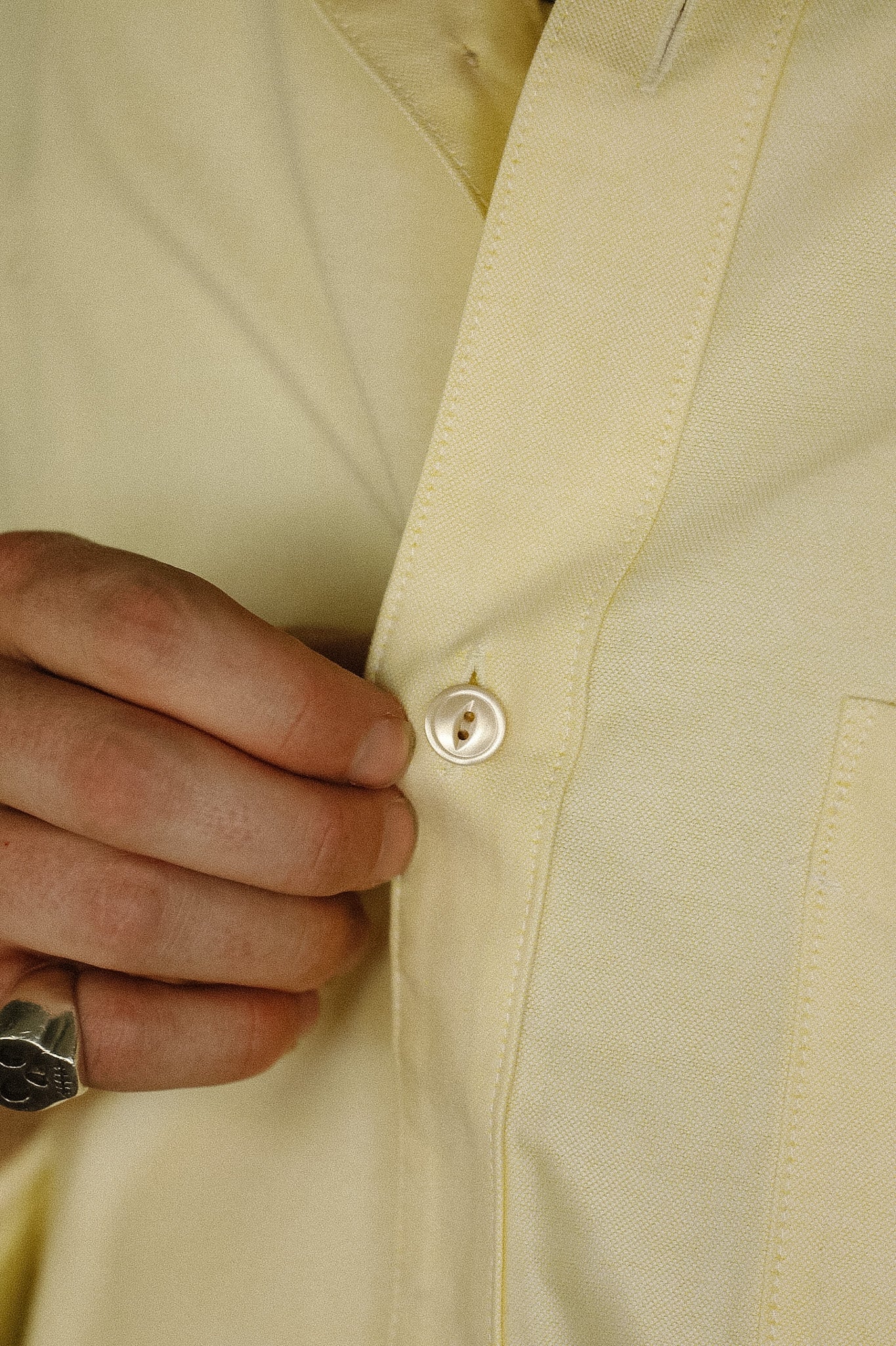 Close-up of a beige jacket with a button being pressed, wearing a ring.
