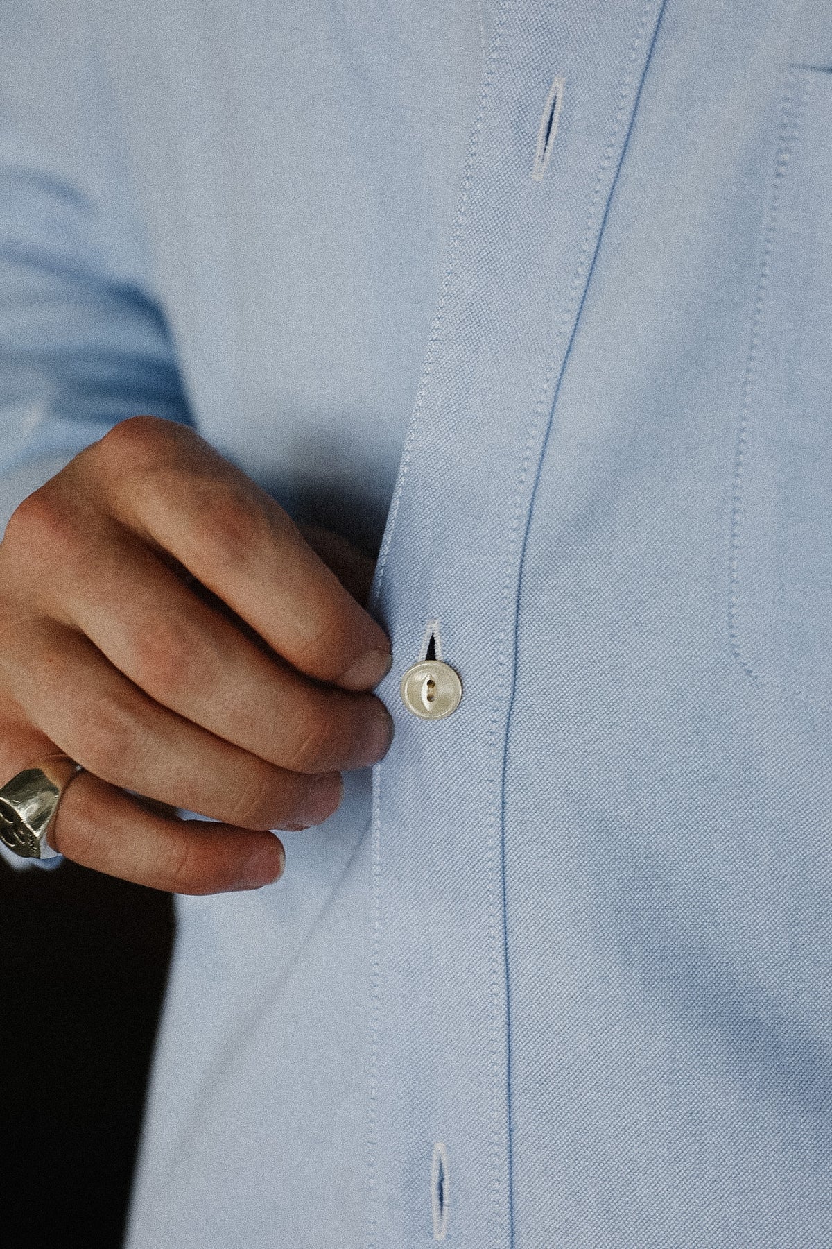 Close-up of a hand buttoning a light blue shirt
