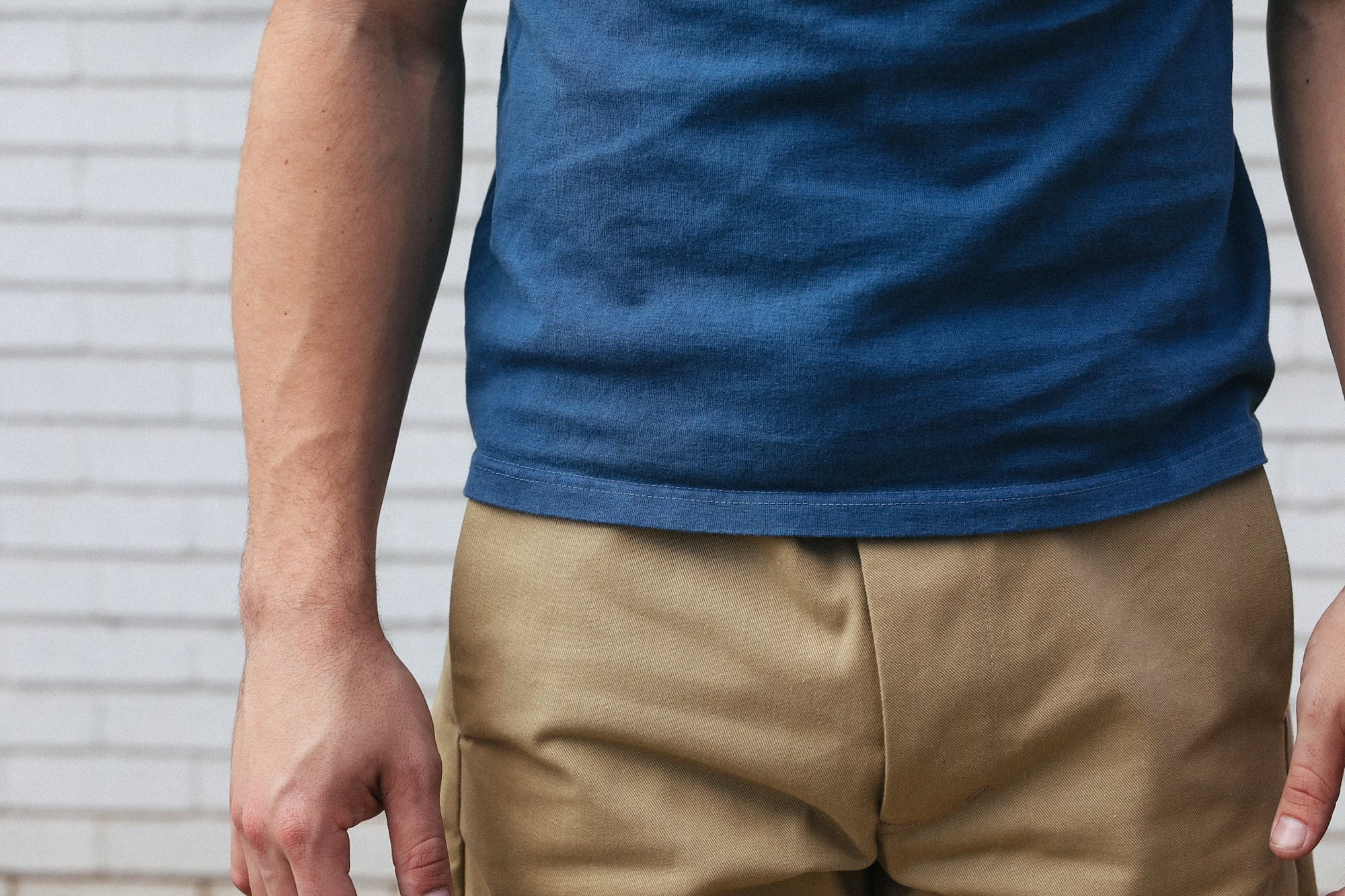 Close-up of a person wearing a blue t-shirt and khaki pants against a white brick wall