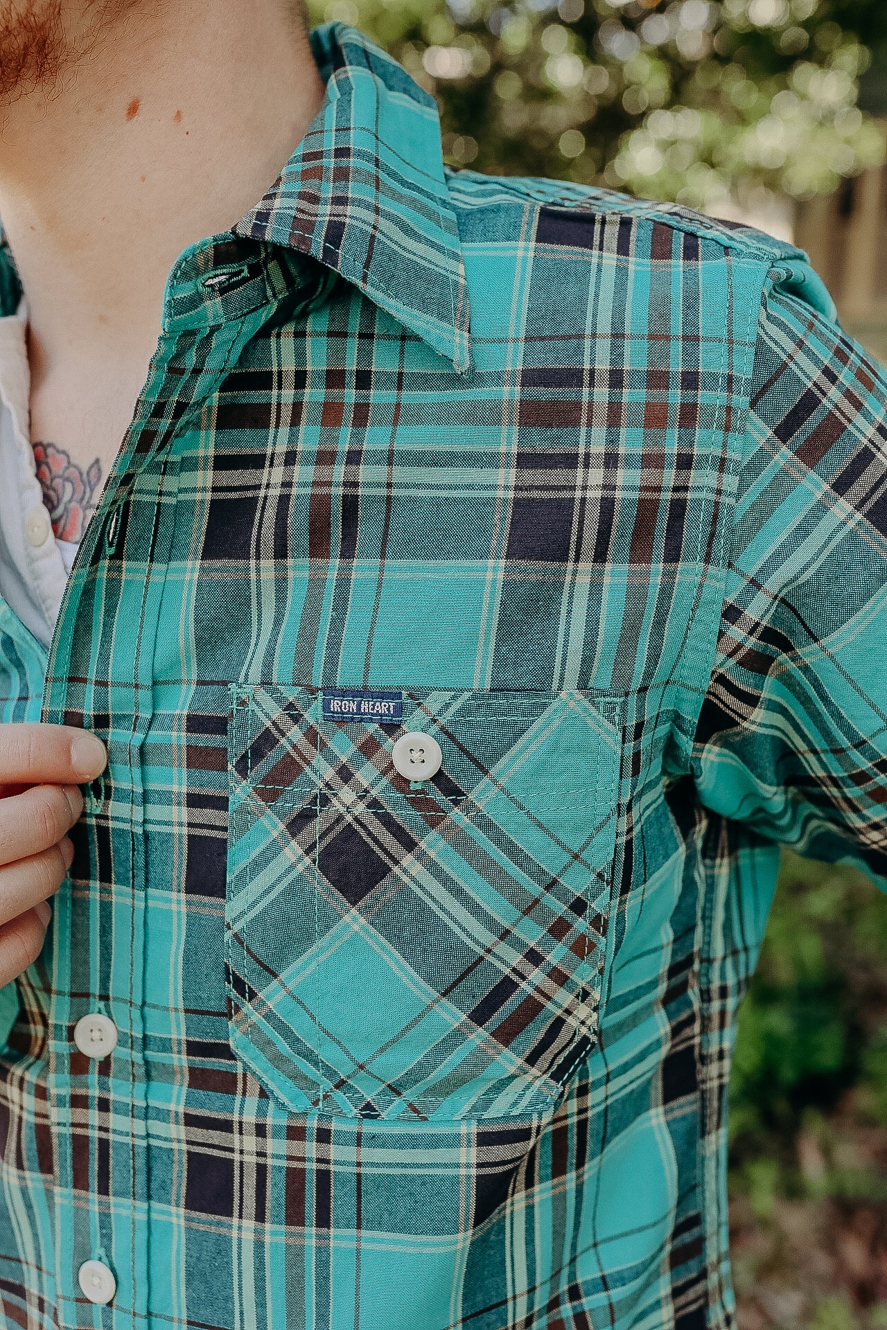 Close-up of teal and navy plaid Iron Heart button-up shirt with pocket detail worn outdoors