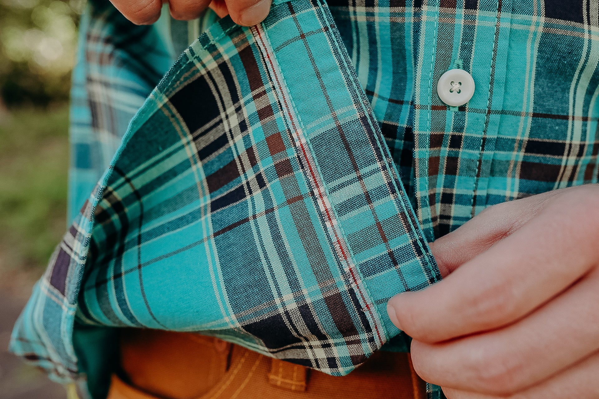 Close-up of a person adjusting a teal plaid button-up shirt, showcasing fabric texture and stitching