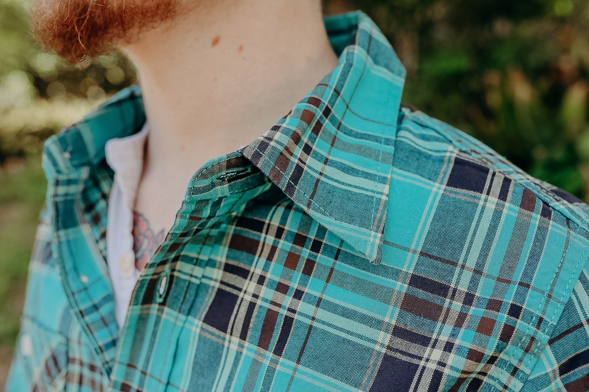 Close-up of a man wearing a turquoise plaid shirt over a white henley shirt outdoors