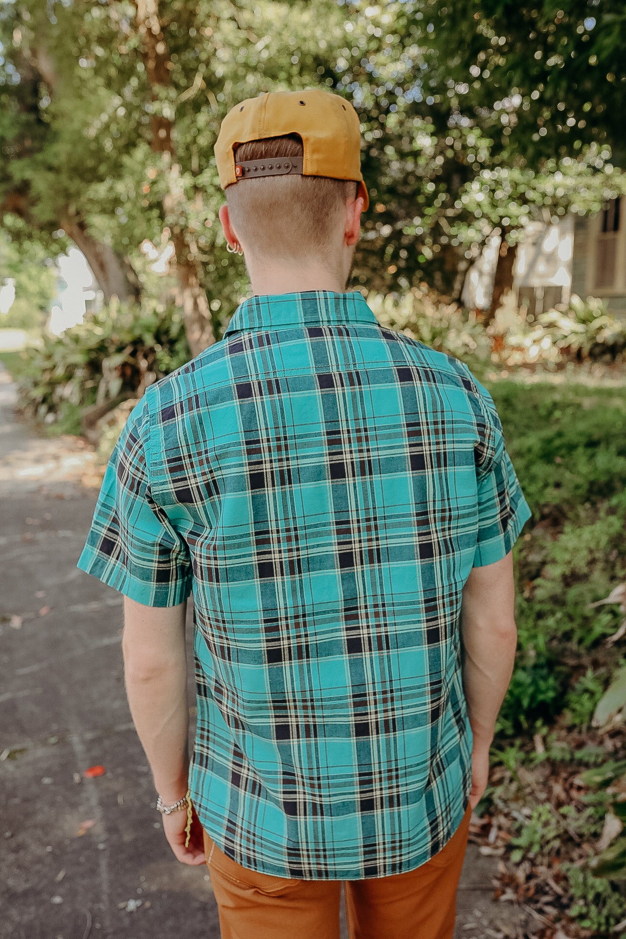Man wearing blue plaid short sleeve shirt and mustard cap outdoors on a sunny day