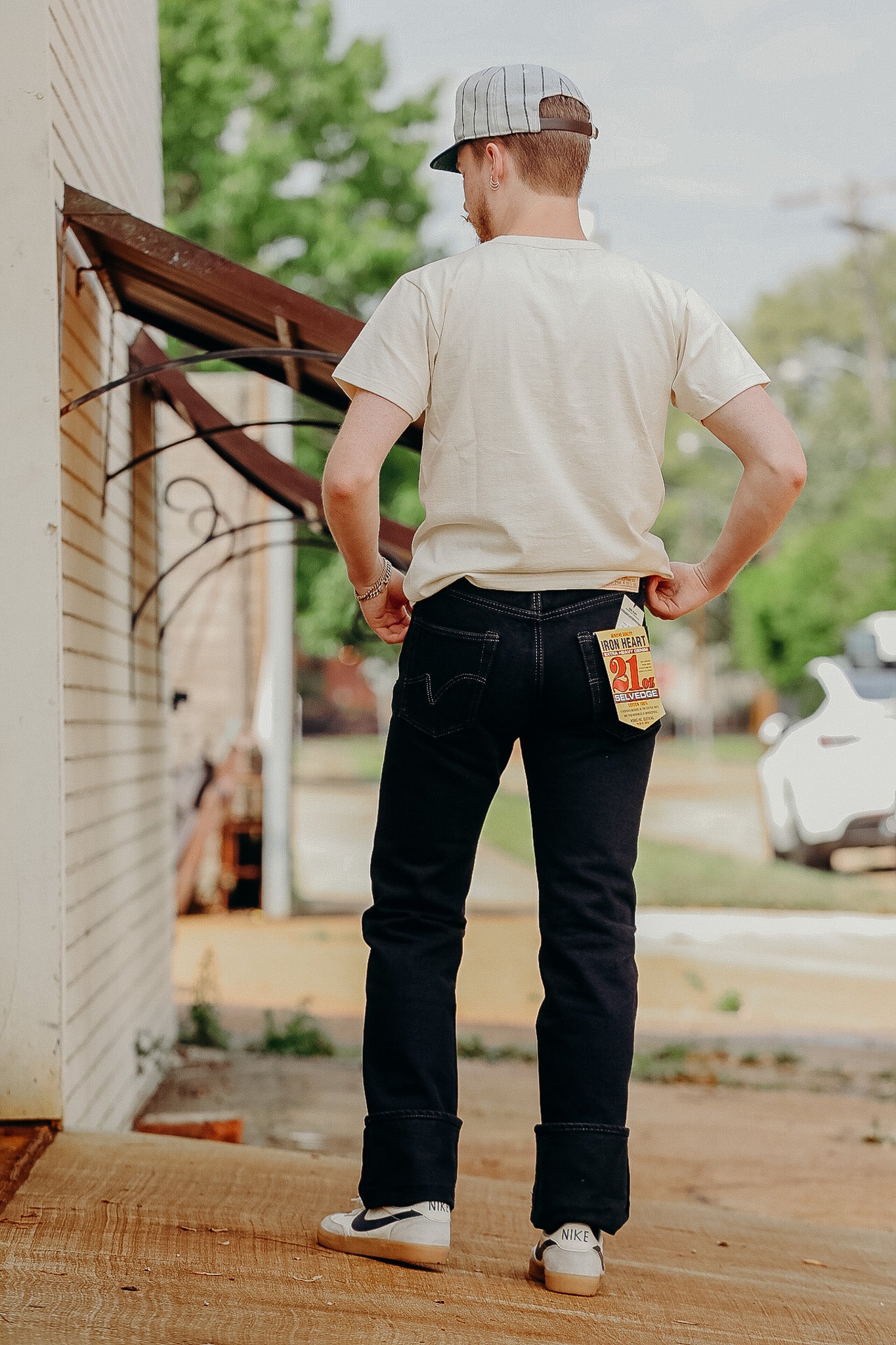 Man wearing black Iron Heart 21oz selvedge denim jeans standing outdoors with beige t-shirt and striped cap