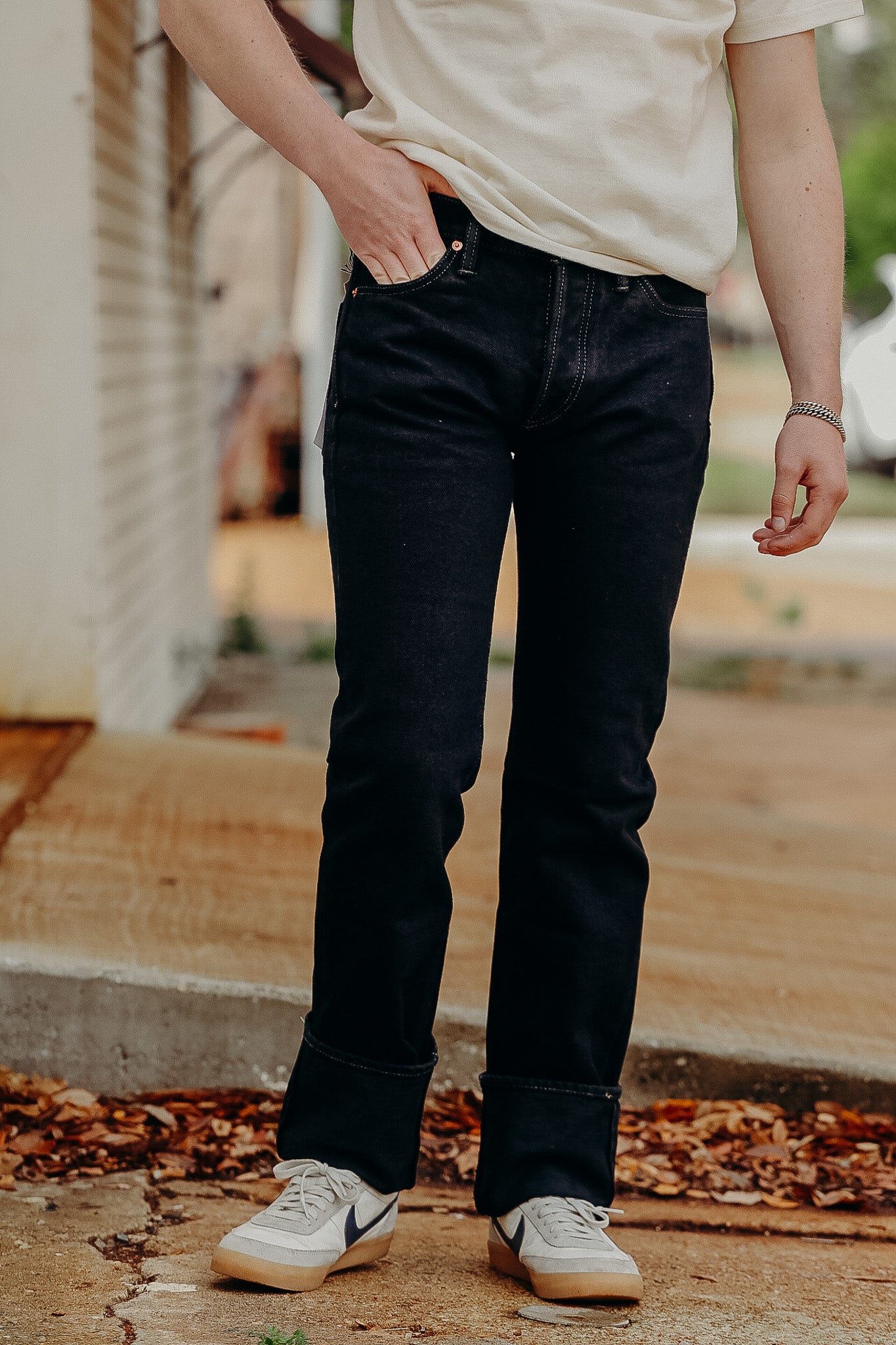 Person wearing black slim fit jeans with cuffed hems and white sneakers outdoors