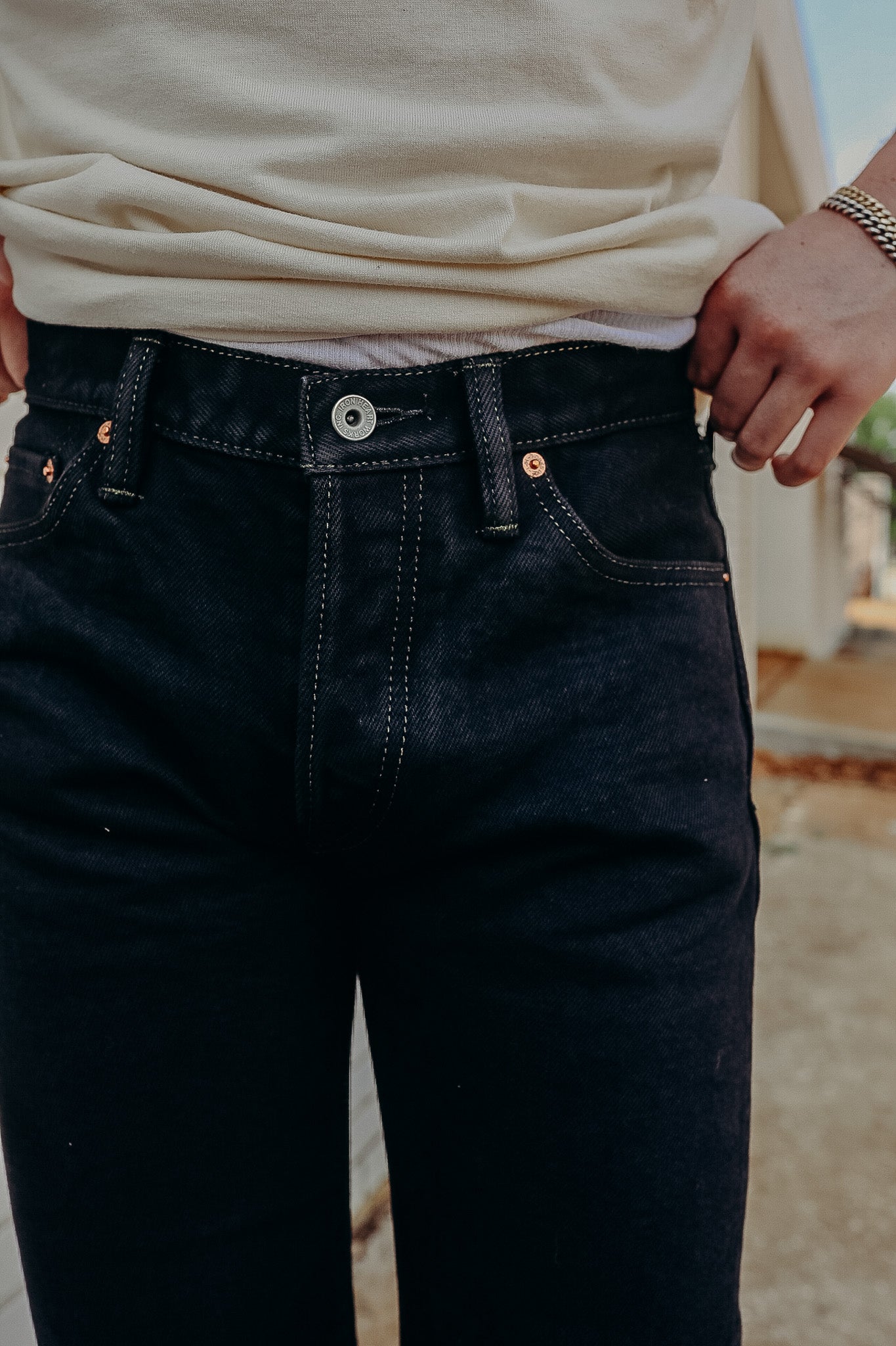 Close-up of person wearing black denim jeans with visible button and light beige shirt tucked slightly in