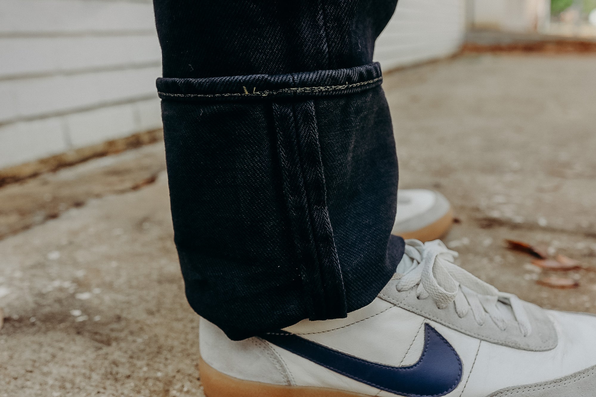 Close-up of rolled-up dark denim jeans paired with white Nike sneakers featuring a blue swoosh logo