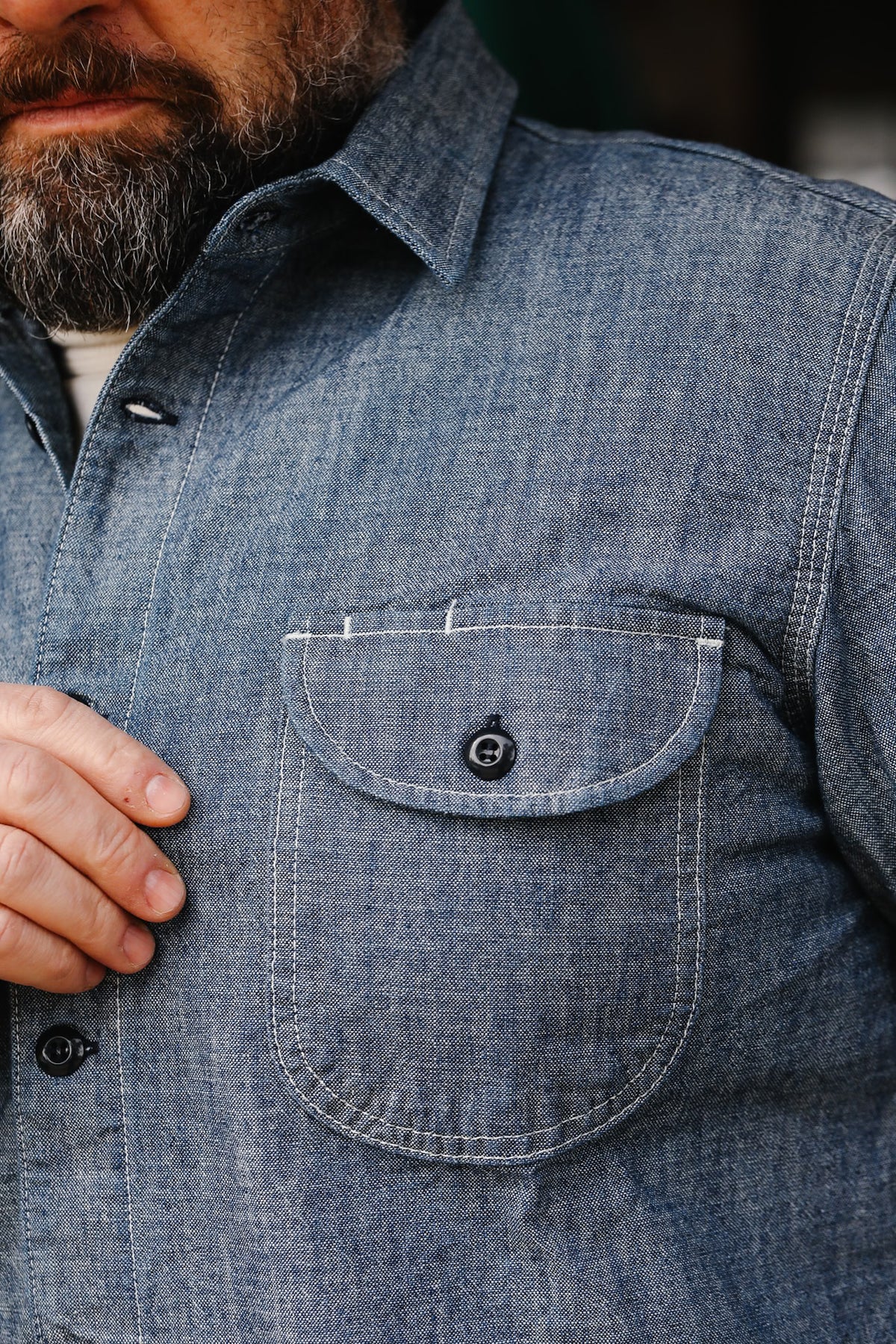 Close-up of man wearing blue chambray work shirt with buttoned chest pocket and beard detail