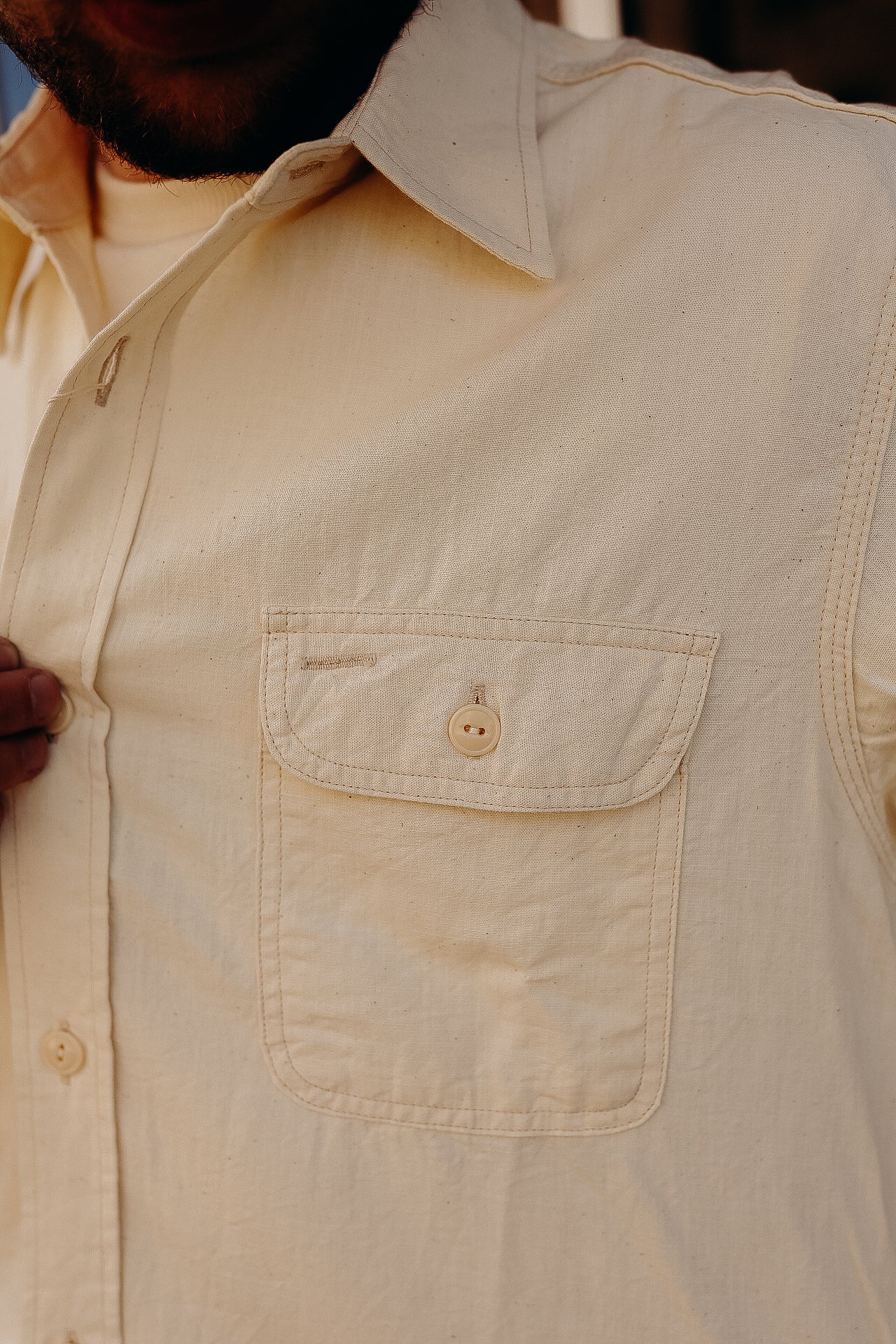 Close-up of man wearing beige button-up long sleeve shirt with chest pocket and collar