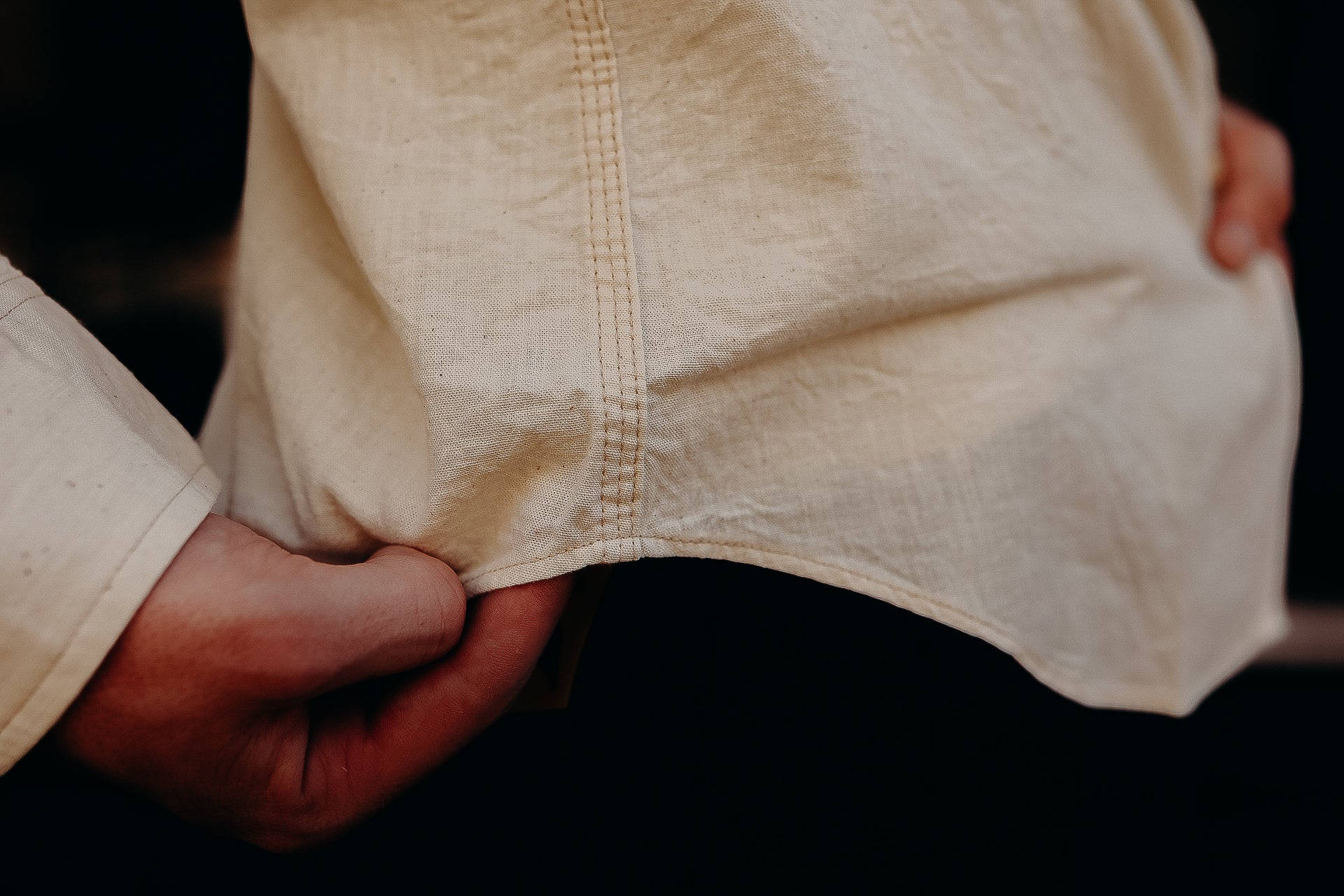 Close-up of hands holding hem of beige work shirt showcasing durable stitching and fabric texture
