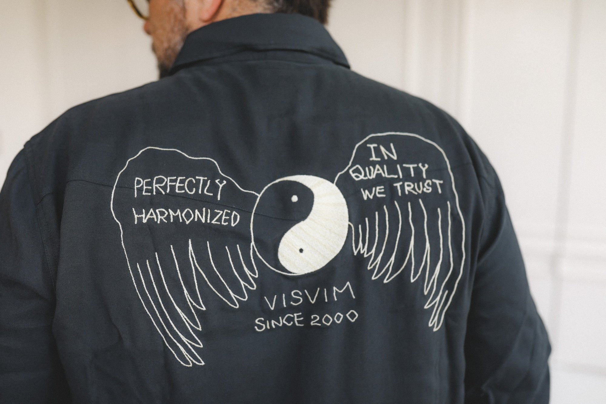 Person wearing a black jacket with white text and graphics on the back, including 'Visvim' branding.