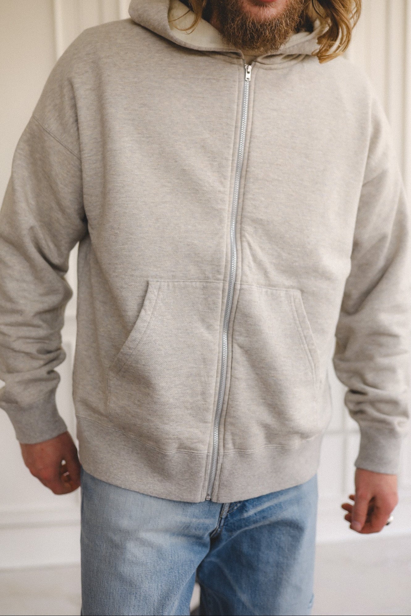 Person wearing a gray zip-up hoodie and blue jeans indoors.