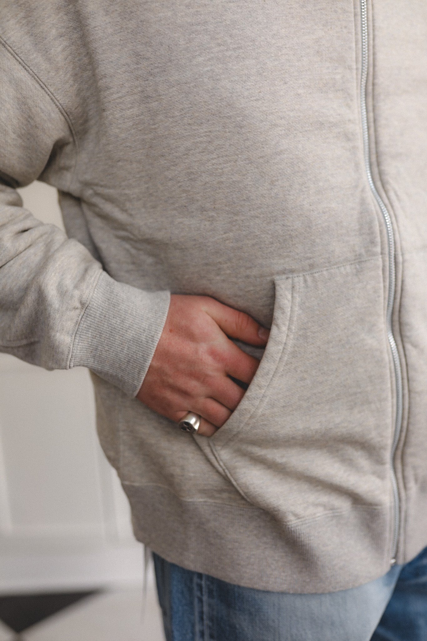 Person wearing a gray hoodie with a zipper, standing indoors.