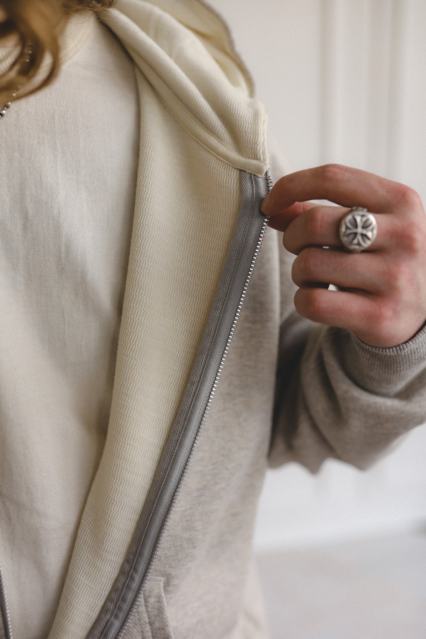 Person zipping a beige jacket with a close-up of the zipper and hand.