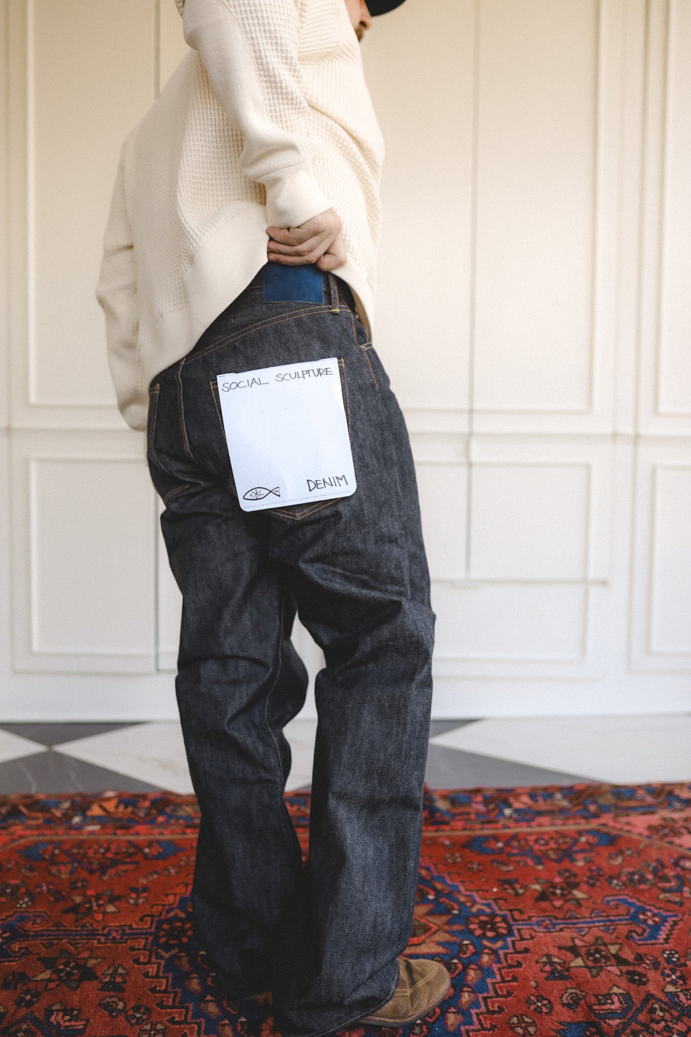 Person wearing dark jeans with a visible brand label on a patterned rug.