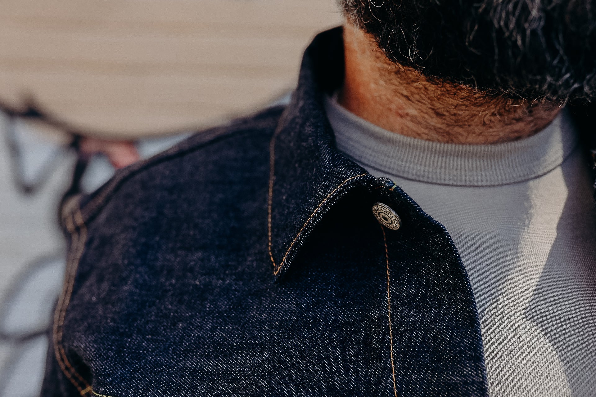 Close-up of a man wearing a dark denim jacket with orange stitching over a light gray shirt, showcasing Iron Shop Provisions style