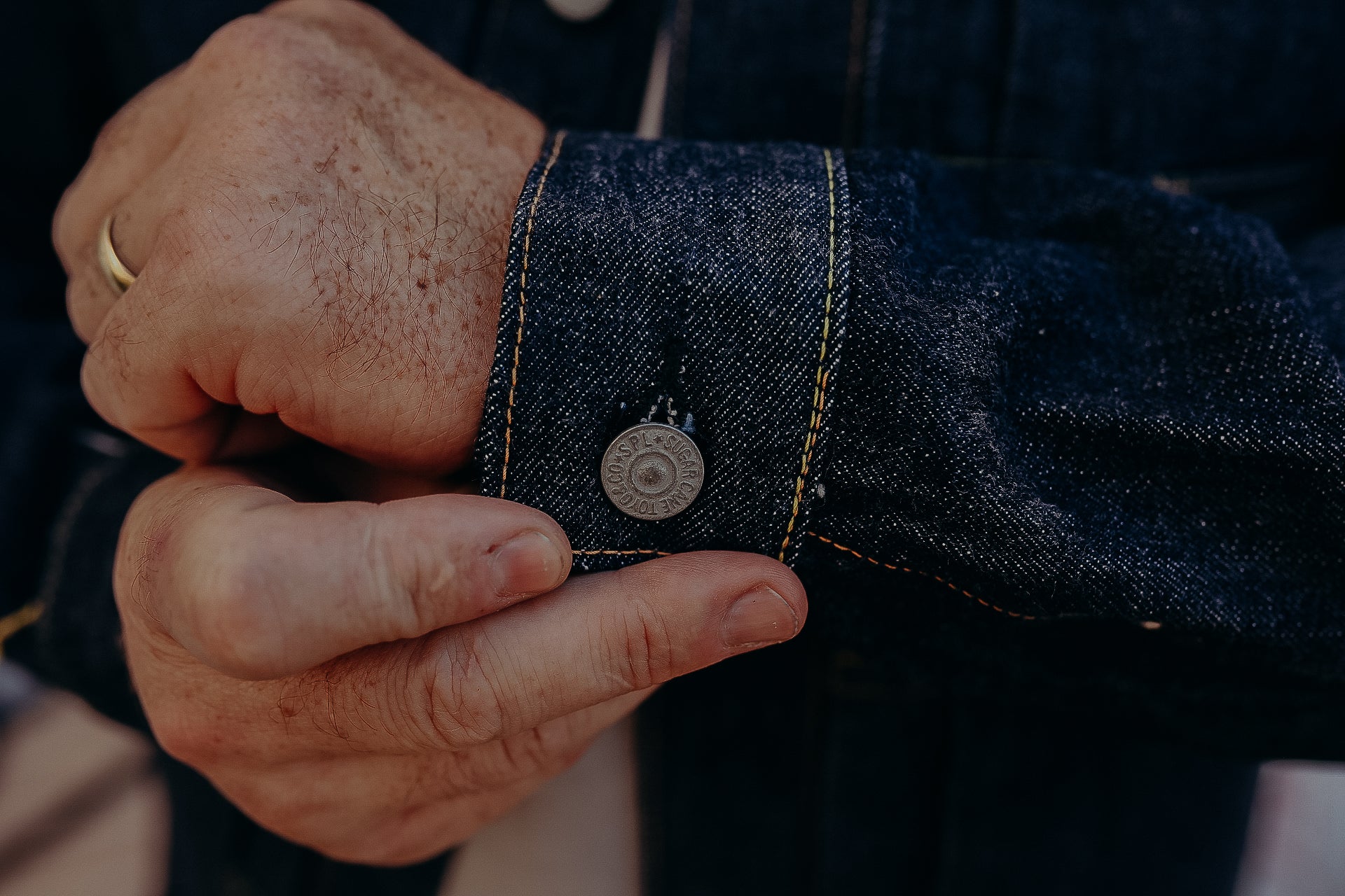 Close-up of a man's hands adjusting the cuff of a dark blue denim jacket with metal button detail
