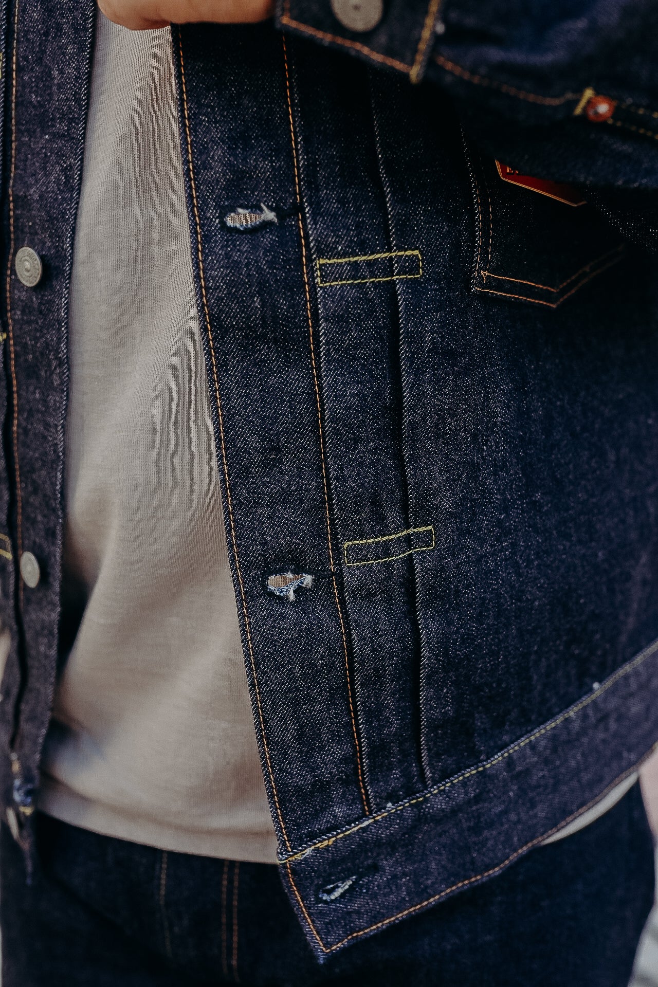 Close-up of person wearing dark blue denim jacket with yellow and orange stitching over beige shirt