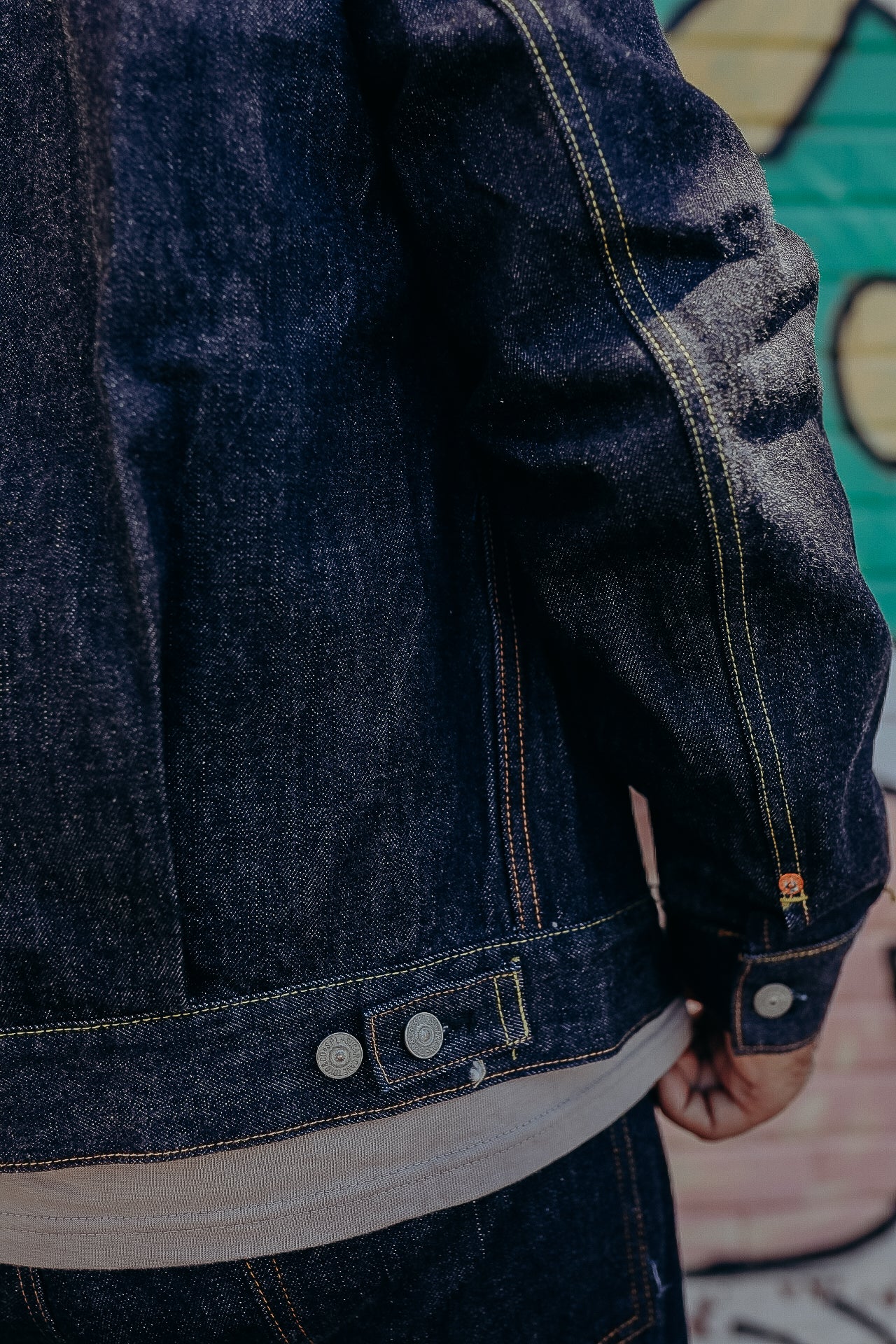 Close-up of dark blue denim jacket with yellow stitching and metal buttons over beige shirt