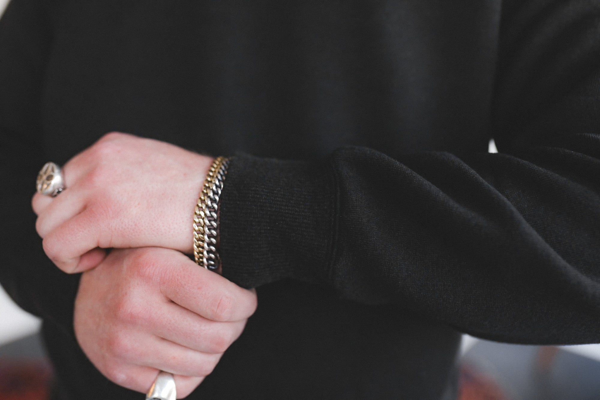 Close-up of a person wearing a black sweater with gold jewelry on a blurred background