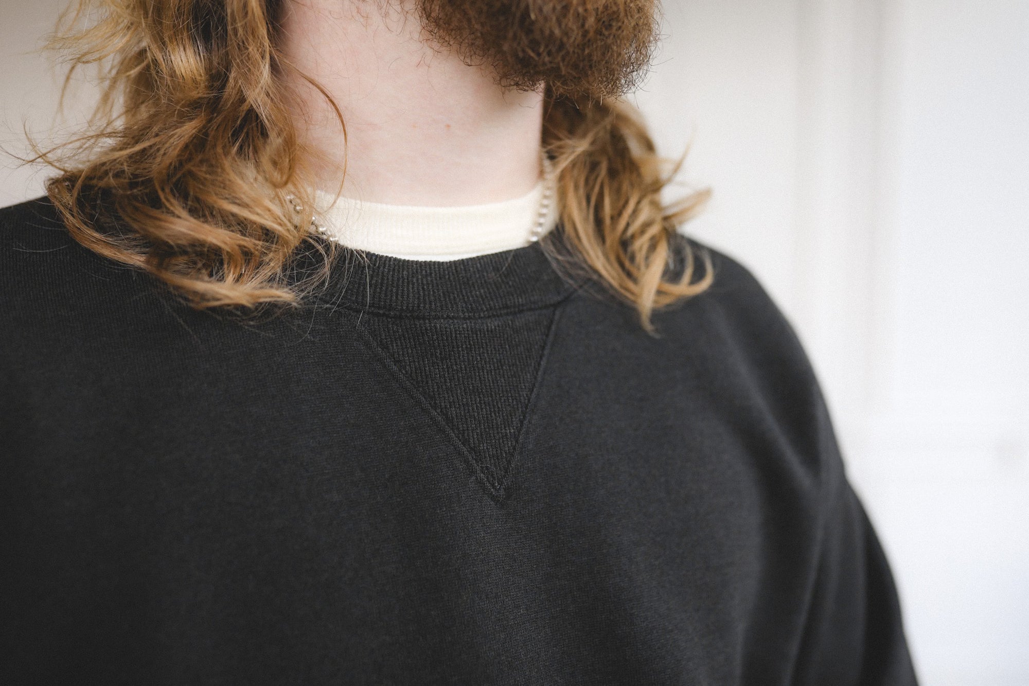 Person wearing a black sweater with a white collar against a neutral background