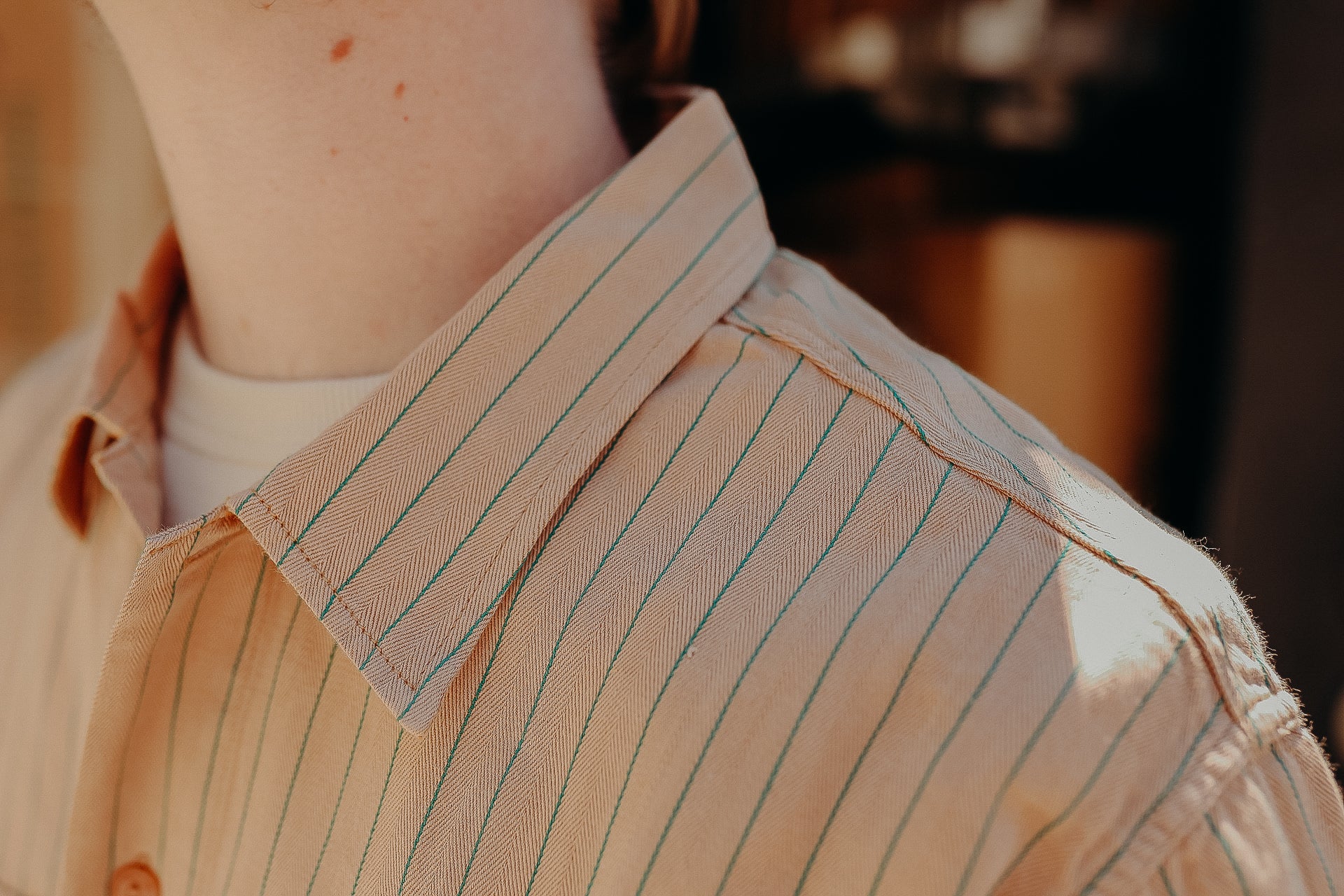 Close-up of a person wearing a cream shirt with green vertical stripes over a white crew neck shirt