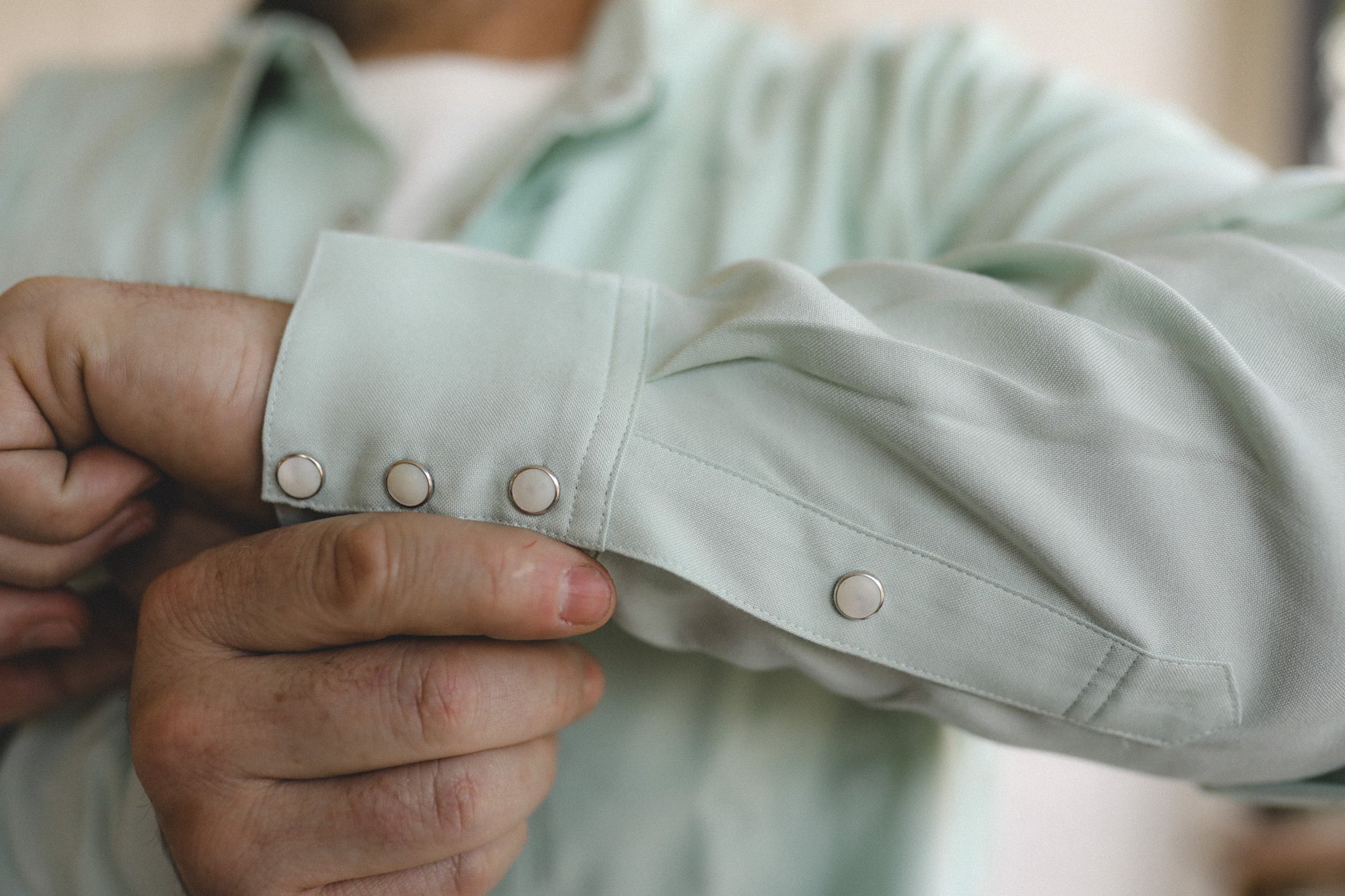 Close-up of a person adjusting the cuff of a light green shirt.
