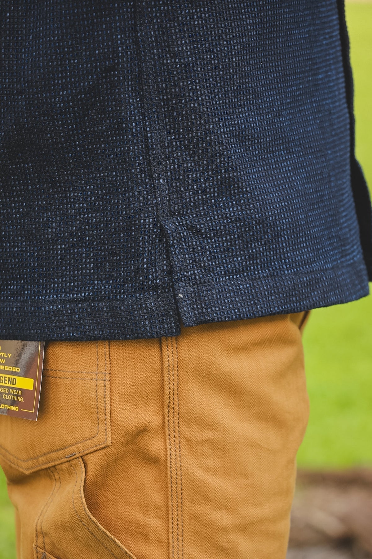 Close-up of a person wearing a navy jacket and brown pants with a blurred green background
