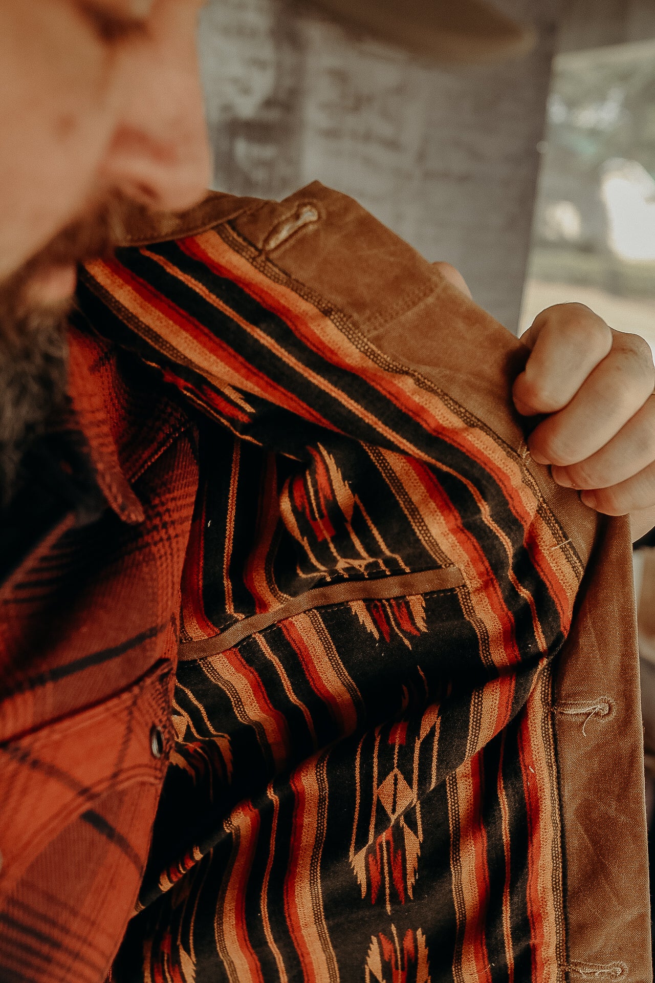 Close-up of man holding open brown jacket showing colorful southwestern patterned lining with geometric designs