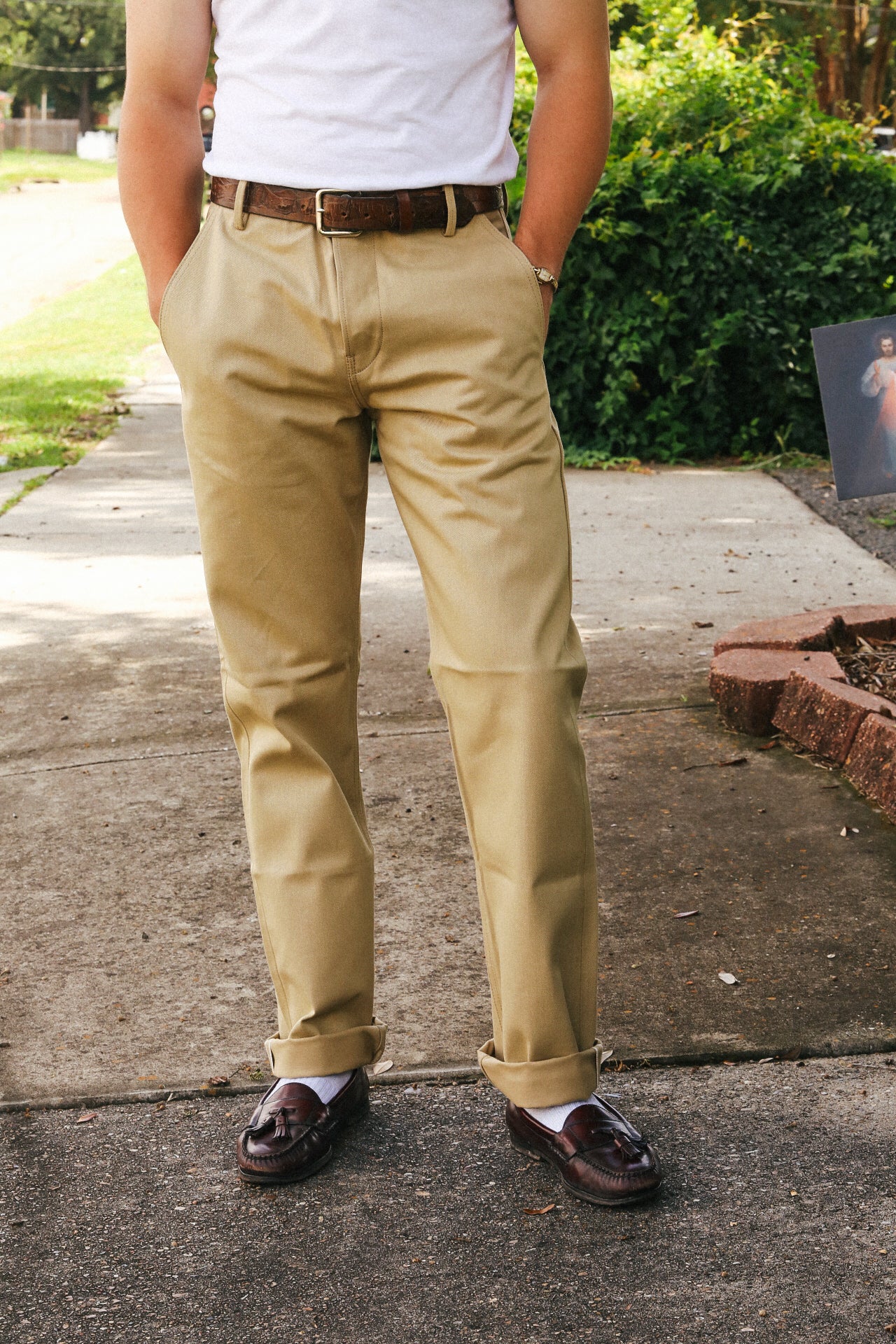 Man wearing rolled-up khaki pants with brown leather belt and dark brown tassel loafers on sidewalk