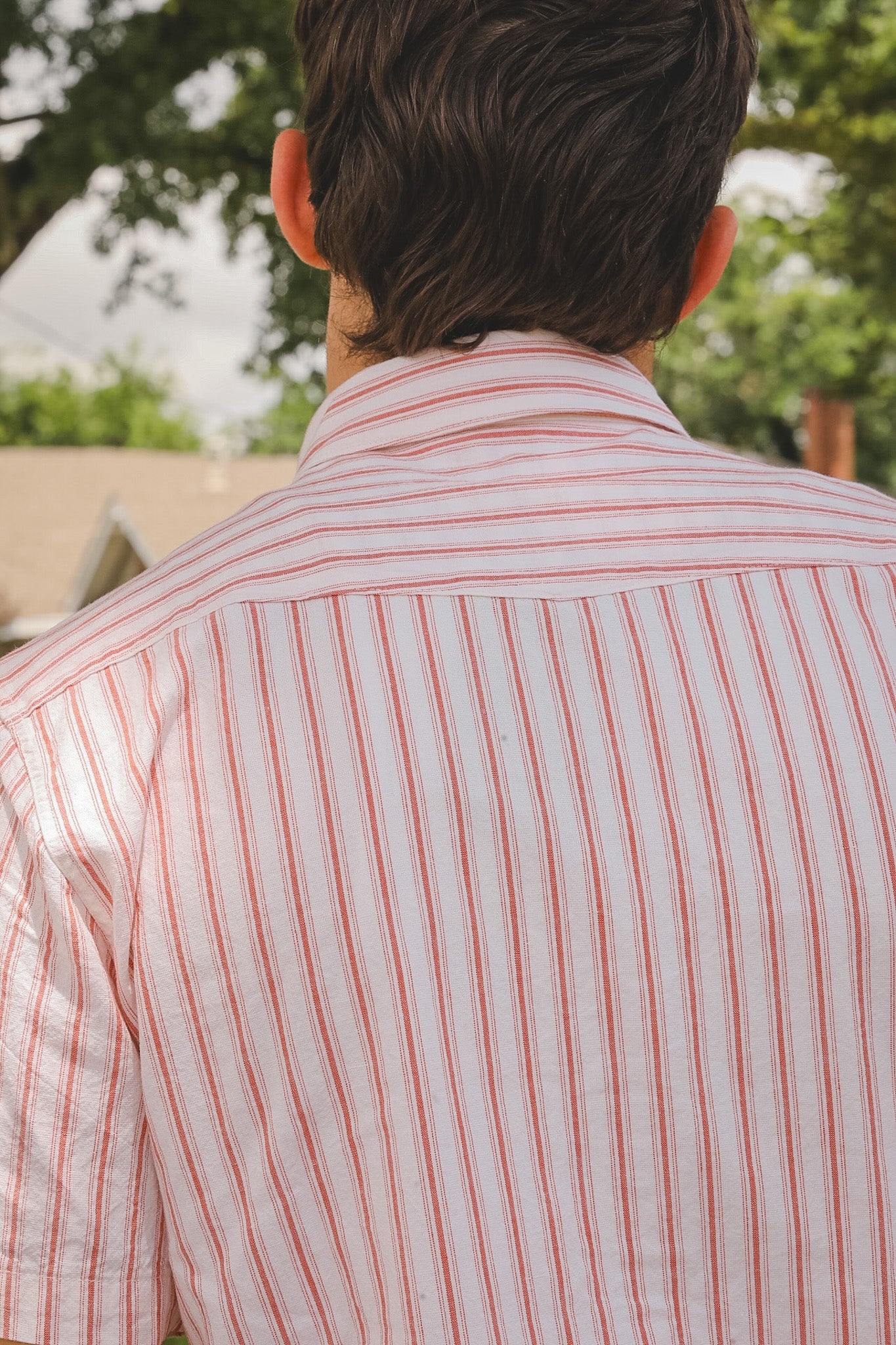 Person wearing a red and white striped shirt with a blurred outdoor background