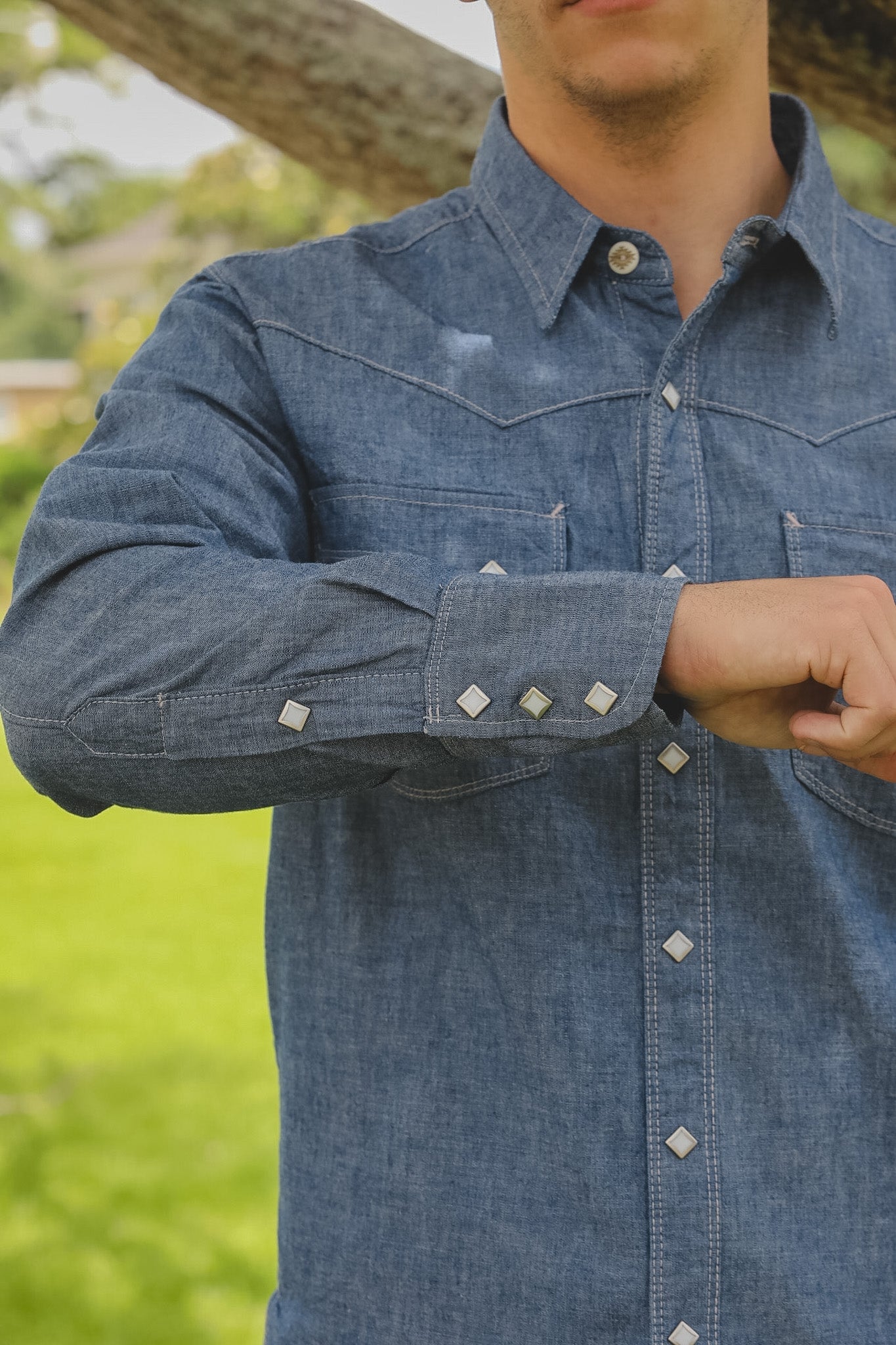 Close-up of a person wearing a blue denim shirt with a blurred green background