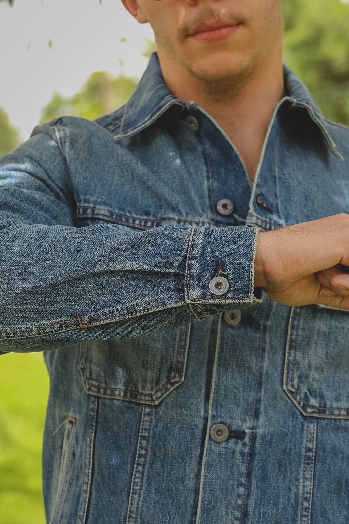 Close-up of a person wearing a blue denim jacket with a blurred green background