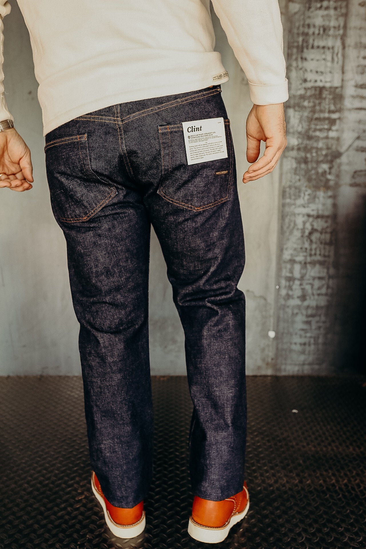 Back view of person wearing dark denim Clint jeans with brown leather boots on industrial floor