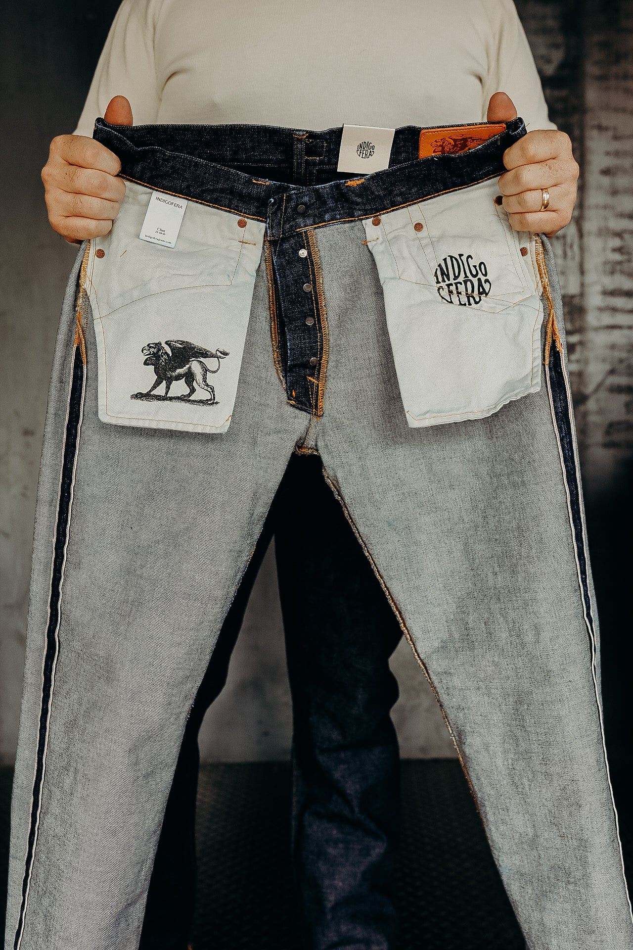 Person holding folded Indigofera selvedge denim jeans showing inside pocket designs and tags