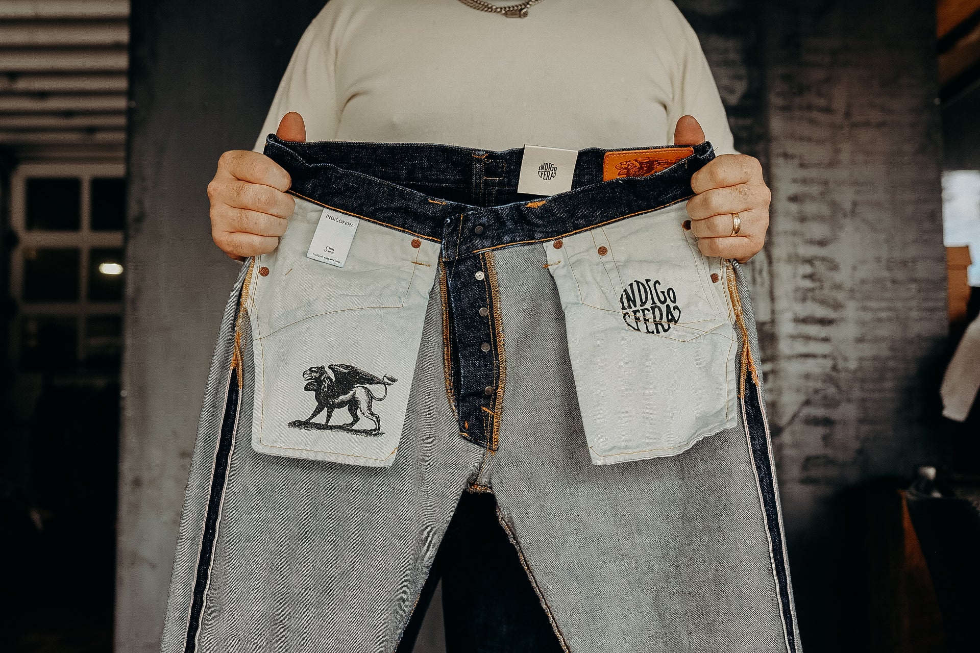 Person holding open Indigofera raw denim jeans showing inside pocket with lion graphic and brand logo