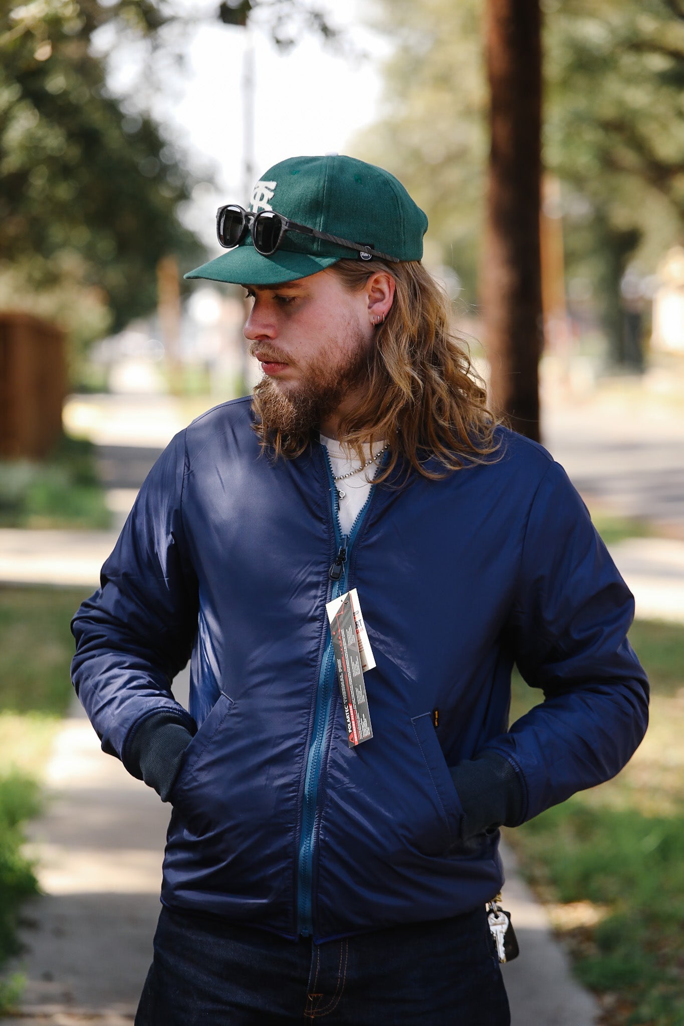 Man wearing a blue jacket and green cap with a camera on his head, standing outdoors.