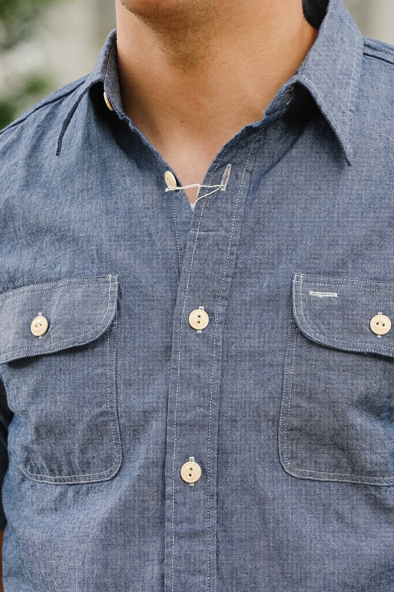 Close-up of a person wearing a blue denim shirt with button details.