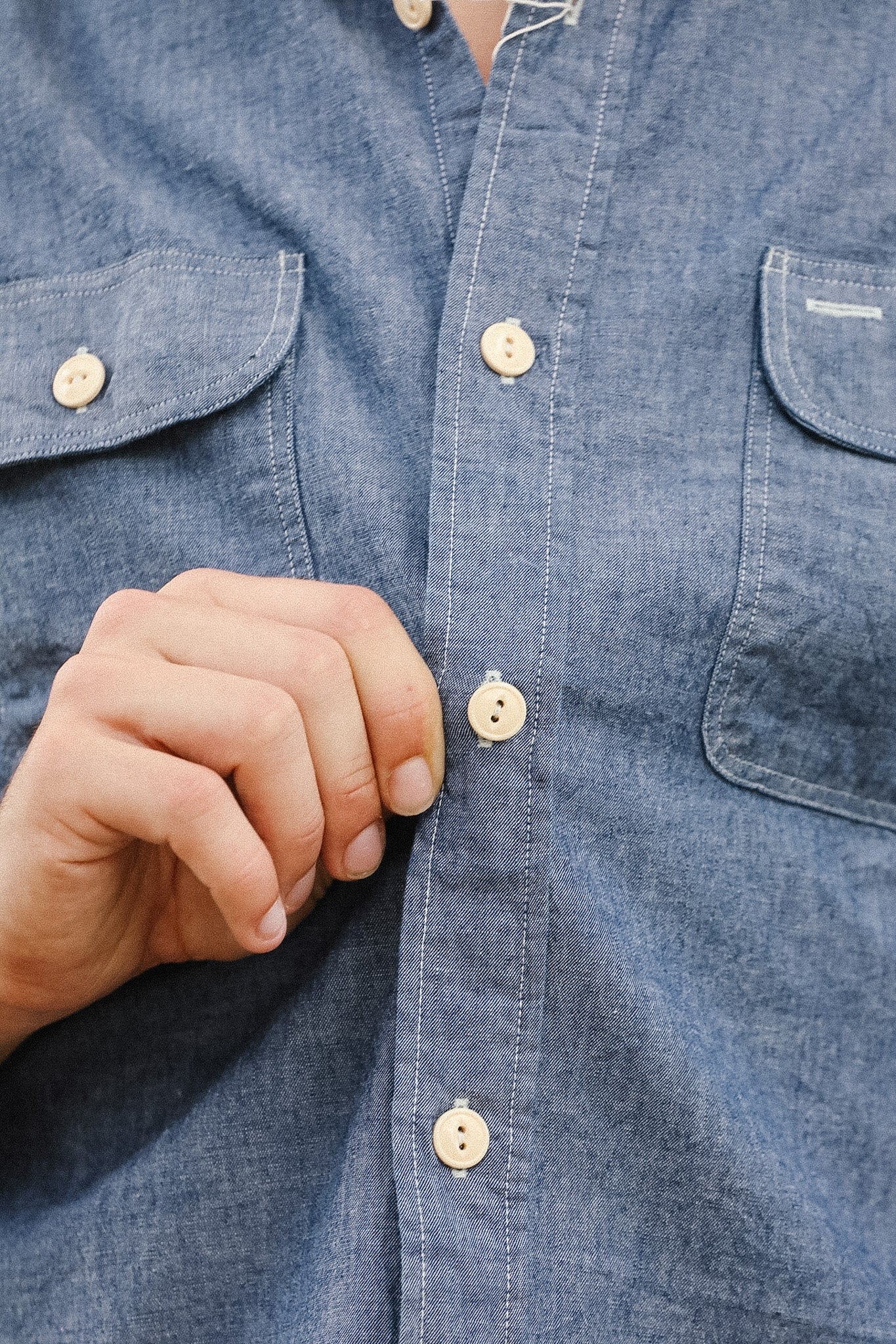 Close-up of a person buttoning a blue denim shirt