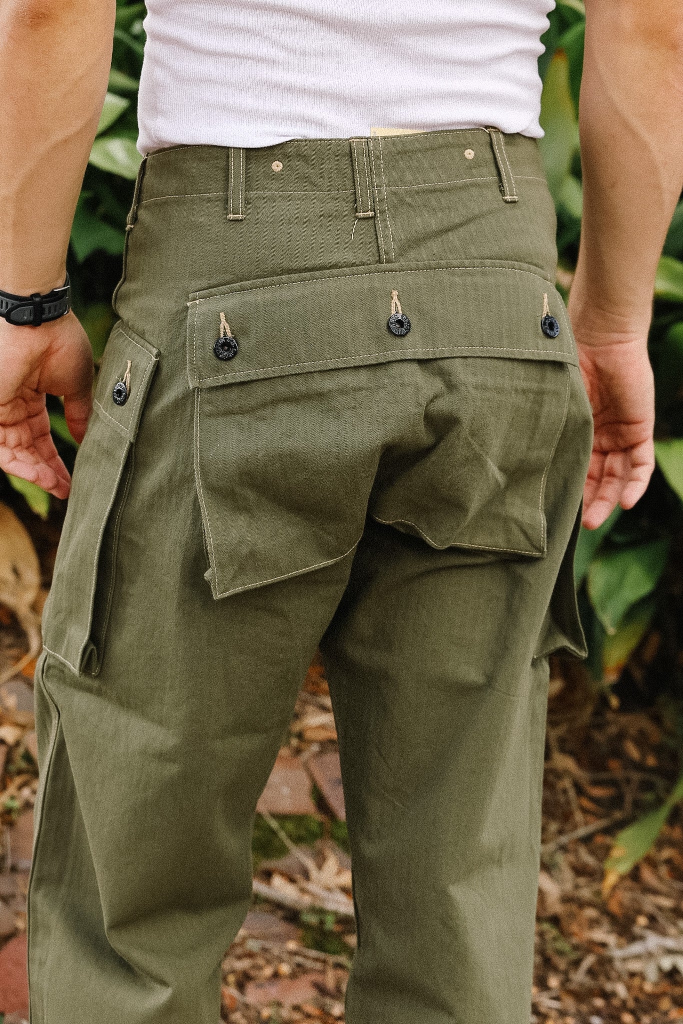 Person wearing olive green tactical pants with multiple pockets outdoors.