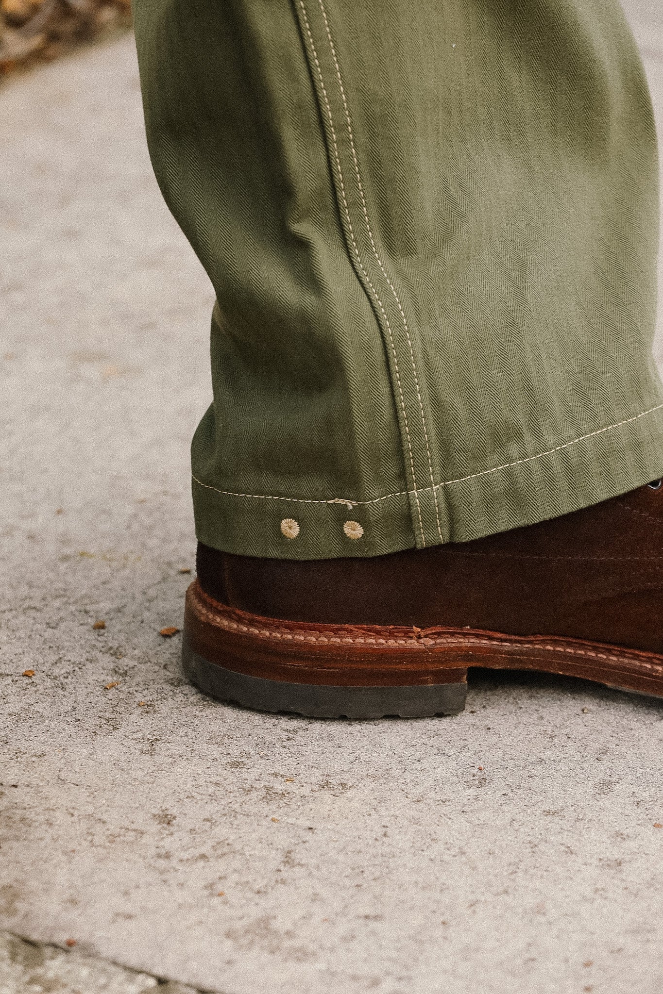 Close-up of green pants with a brown boot on a concrete surface