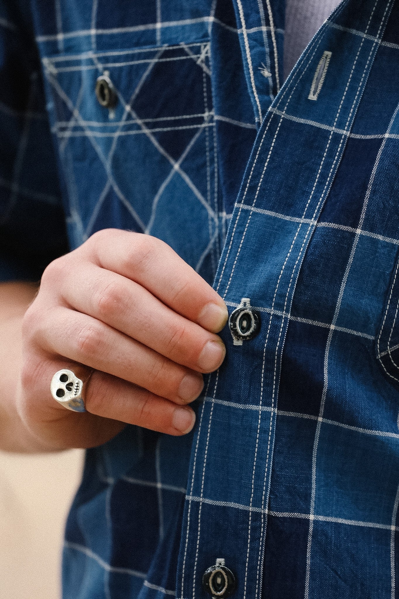 Close-up of a hand buttoning a blue plaid shirt with a ring on the finger.