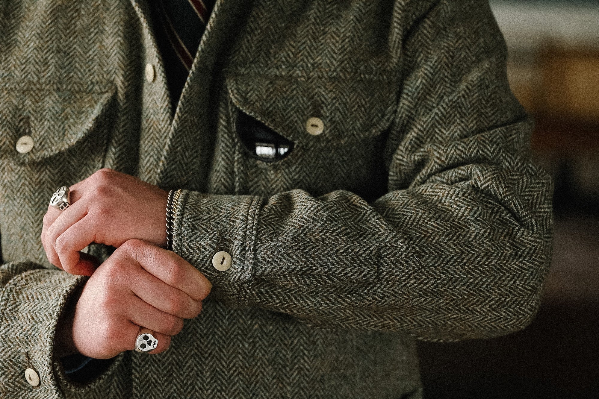 Person wearing a green herringbone jacket with visible buttons and cuffs.